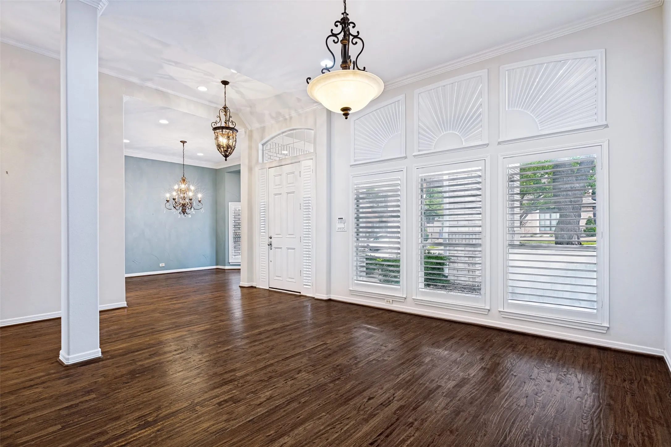 Dramatic foyer featuring soaring ceilings, elegant lighting, and rich, wide-plank hardwood floors. The formal living room, accented by exquisite millwork and column details, offers an ideal space for hosting guests.