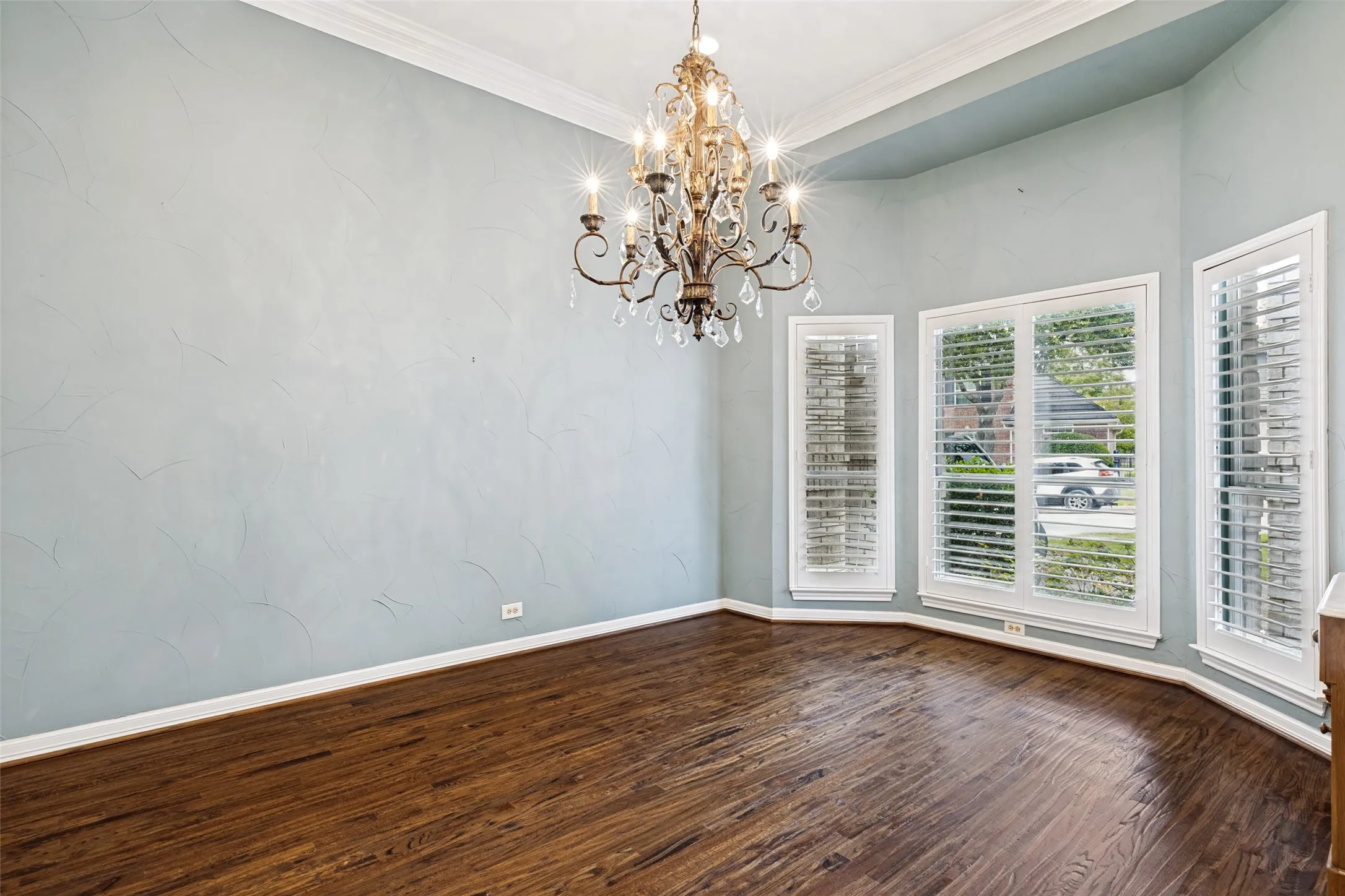 Formal dining room featuring an elegant chandelier, crown molding, and plantation shutters. This space offers a seamless flow to the living area and convenient direct access to the kitchen for effortless entertaining.