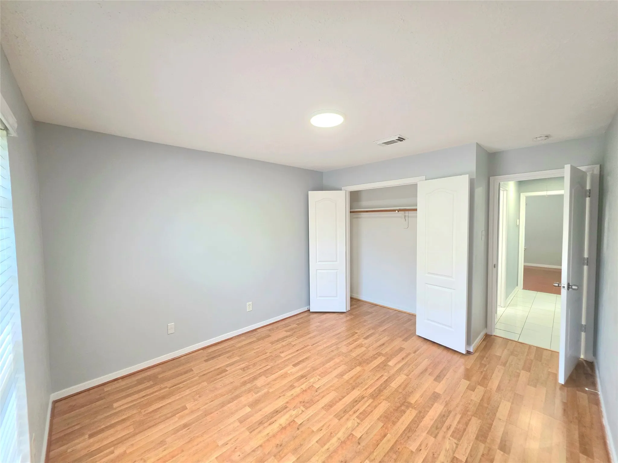 Spacious room featuring wood-finish flooring, light blue wall paint, white trim, and a built-in closet with bifold doors