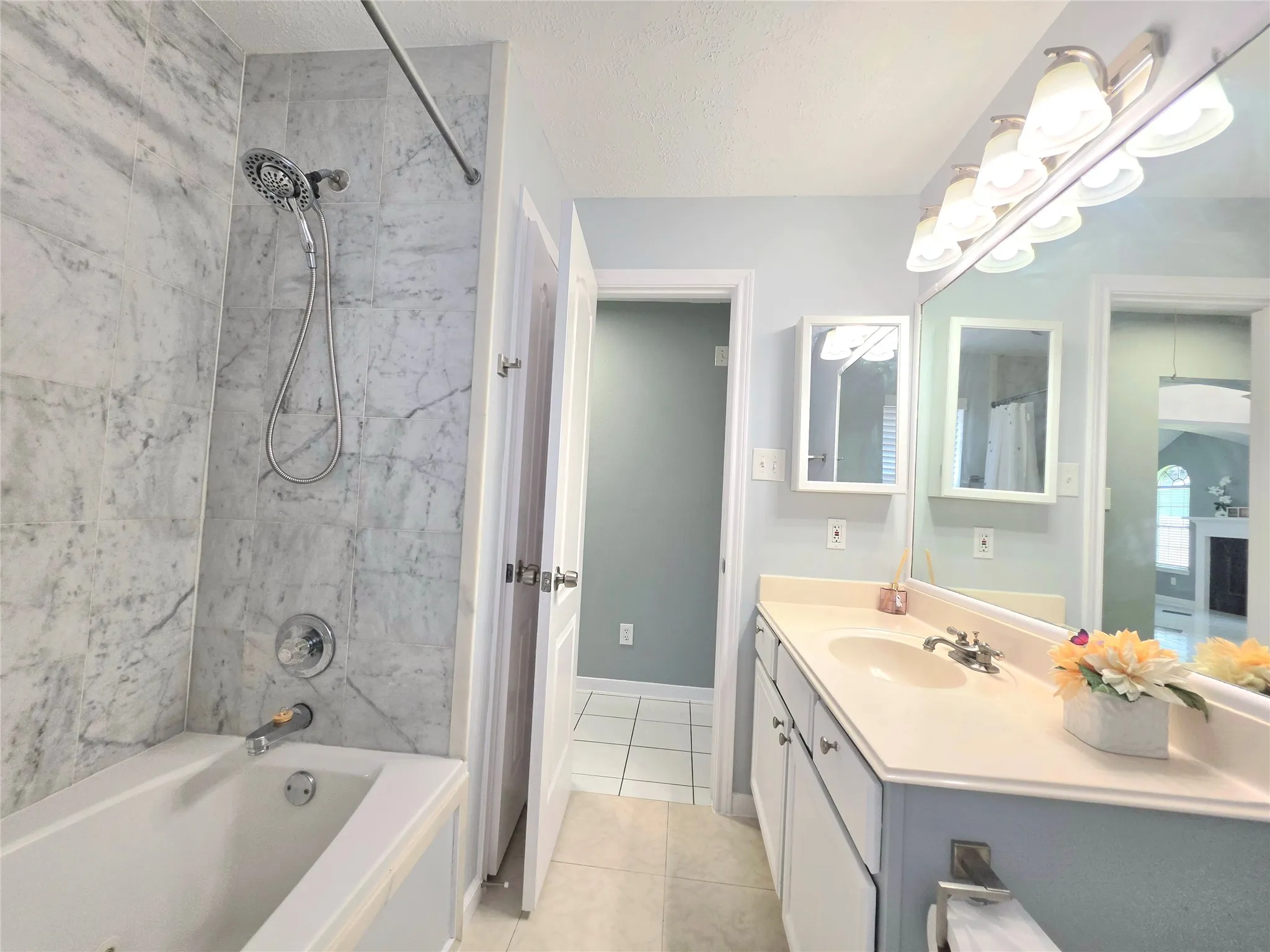 Bathroom featuring a tub/shower combination with large format tiled surround, a double vanity with an integrated countertop and dual sinks, and a large wall-mounted mirror