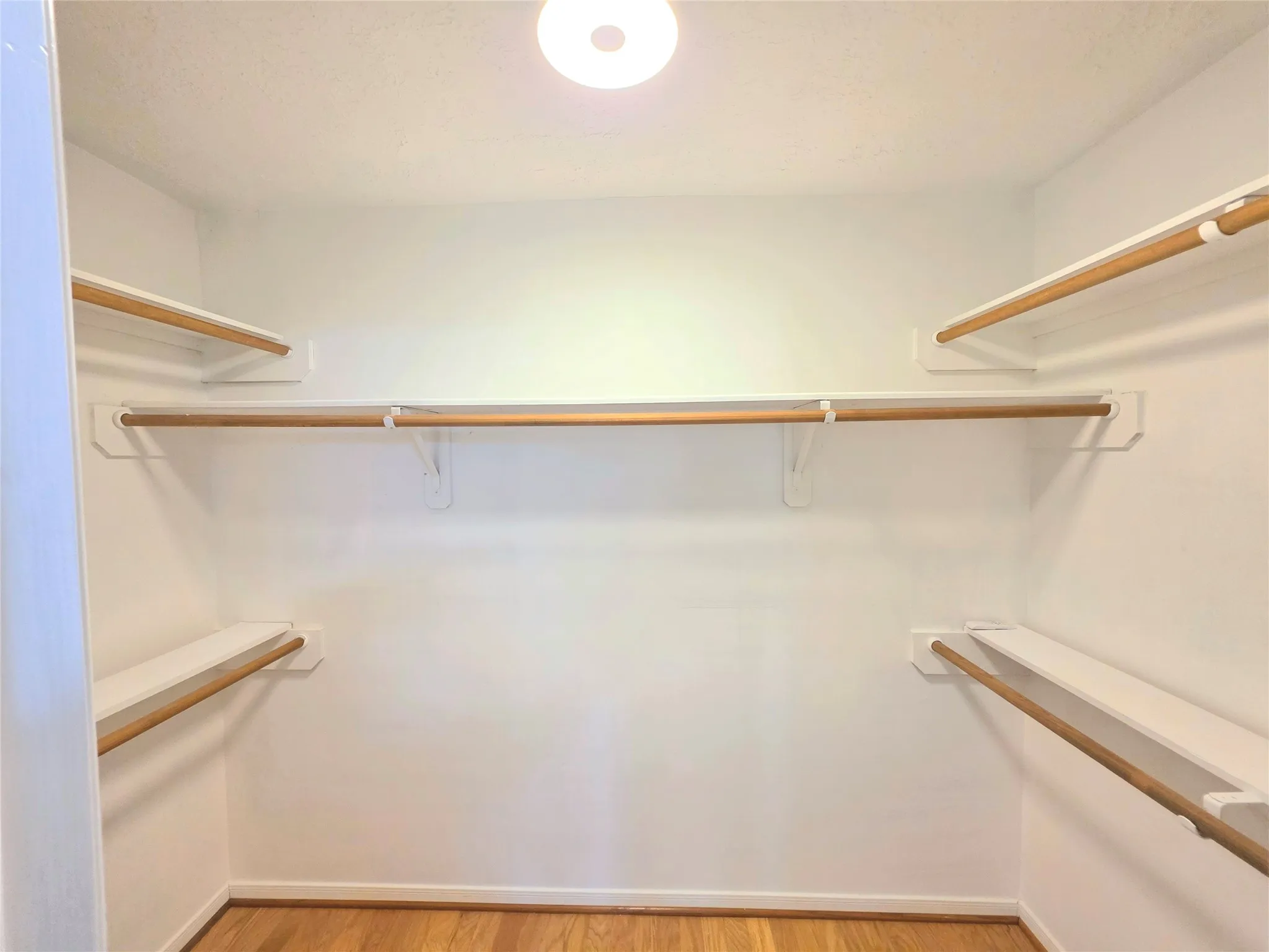 Walk-in closet featuring hardwood flooring, white shelving, and multiple hanging rods