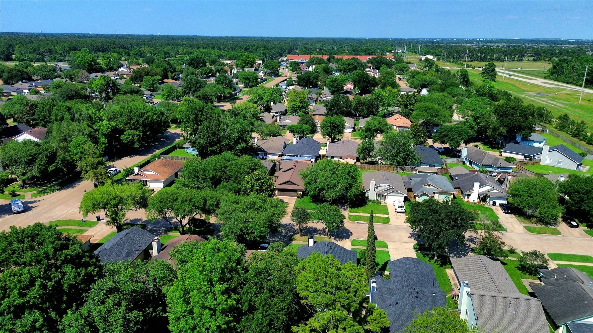 Expansive aerial capturing a residential area with numerous single-family homes, mature tree canopy, varied roofing styles, and visible roadways