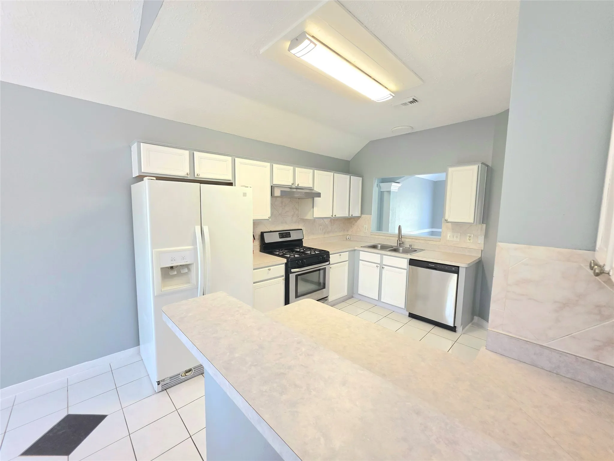 Kitchen featuring white cabinetry, light-toned countertops, a stainless steel dishwasher, a gas range, and white tiled flooring