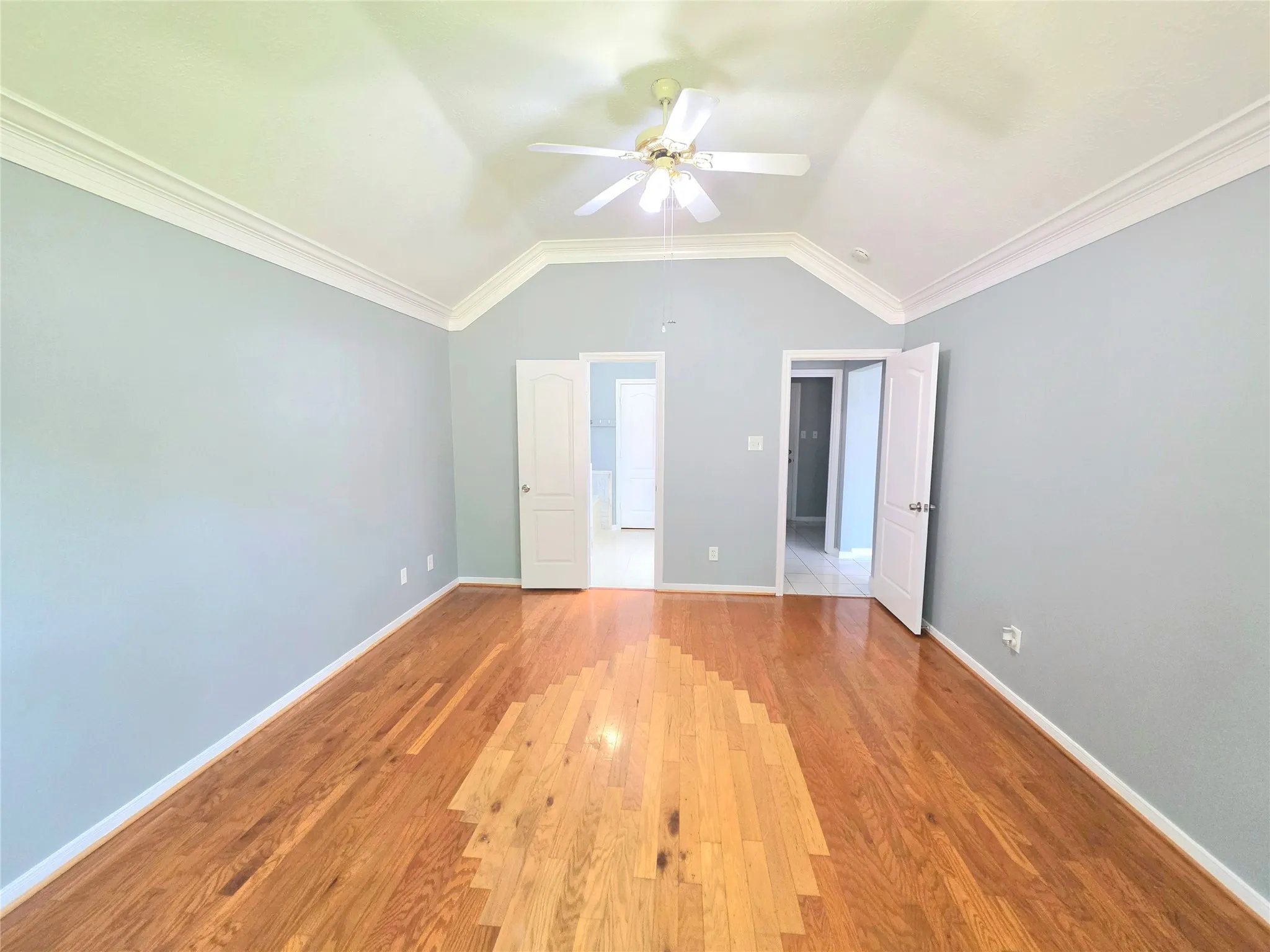 Hardwood flooring throughout featuring light blue walls, a vaulted ceiling, a ceiling fan, and crown molding