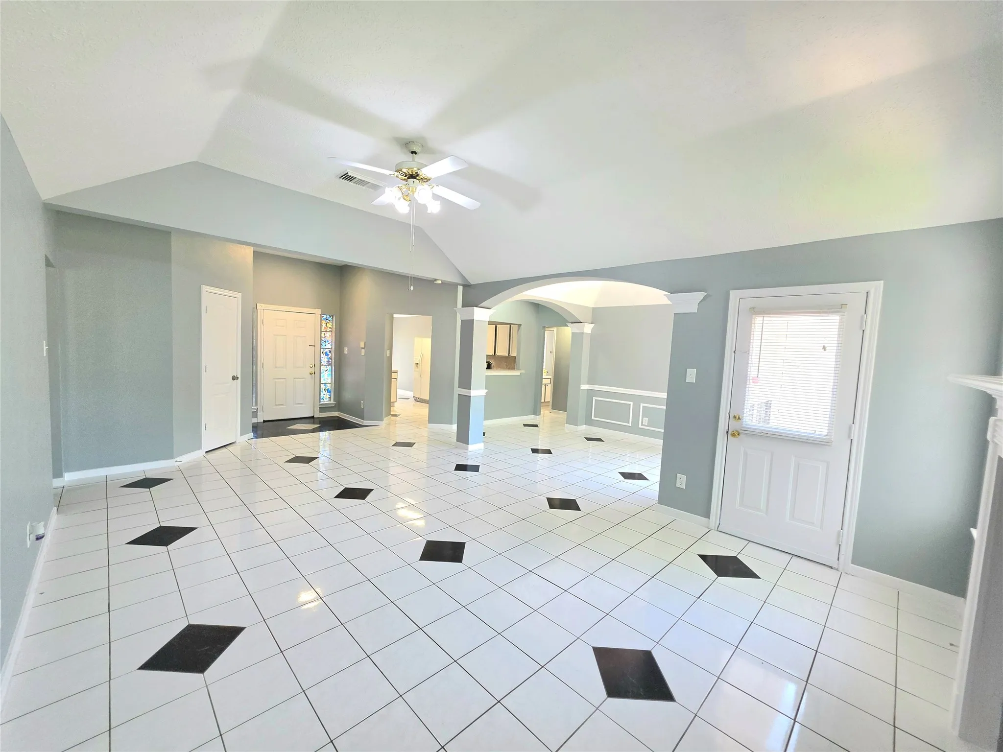 Spacious living area featuring white tile flooring with black diamond accents, a vaulted ceiling, and a ceiling fan