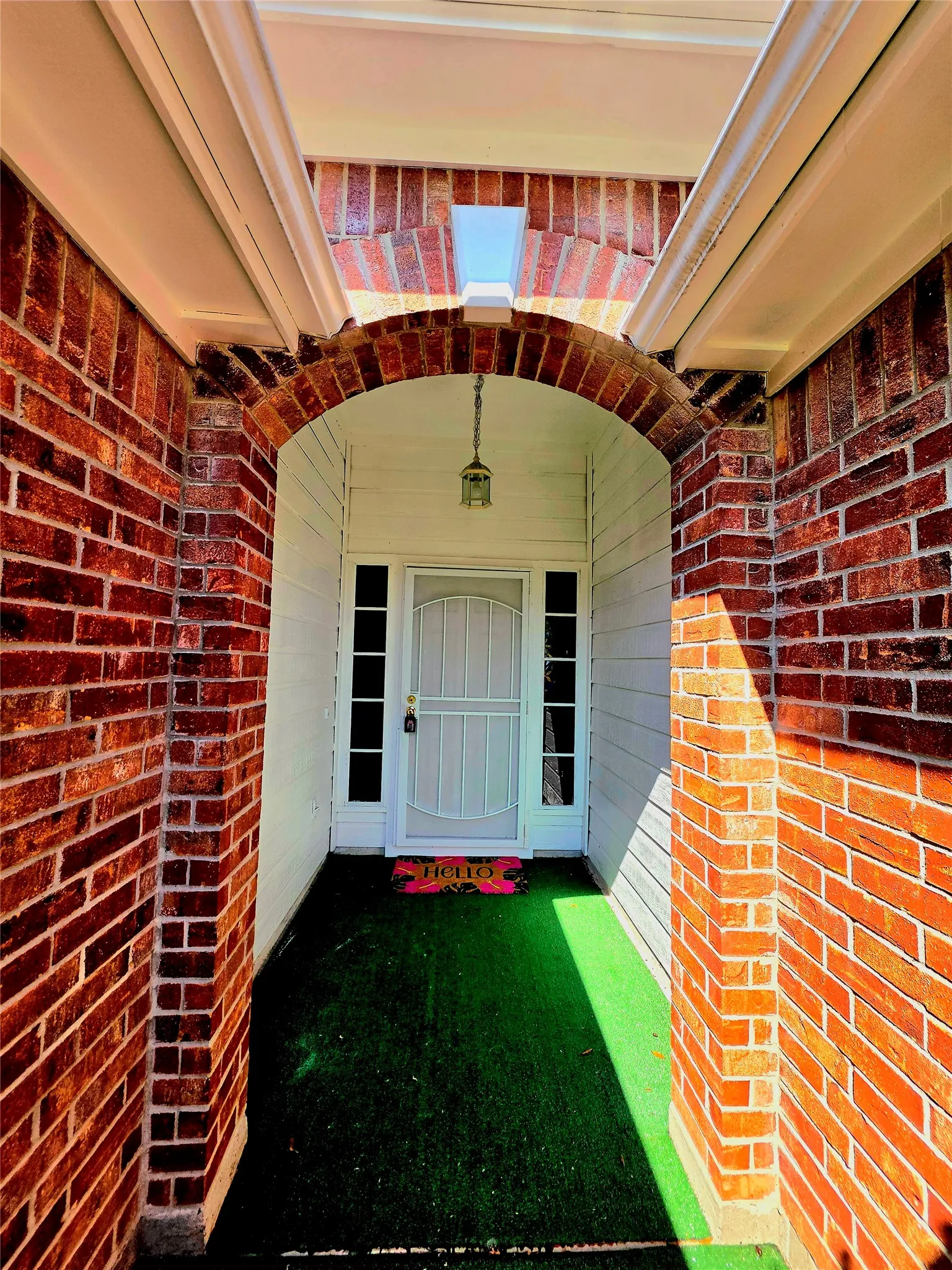 Brick archway entry featuring a white paneled door, sidelight windows, and a hanging outdoor lantern fixture