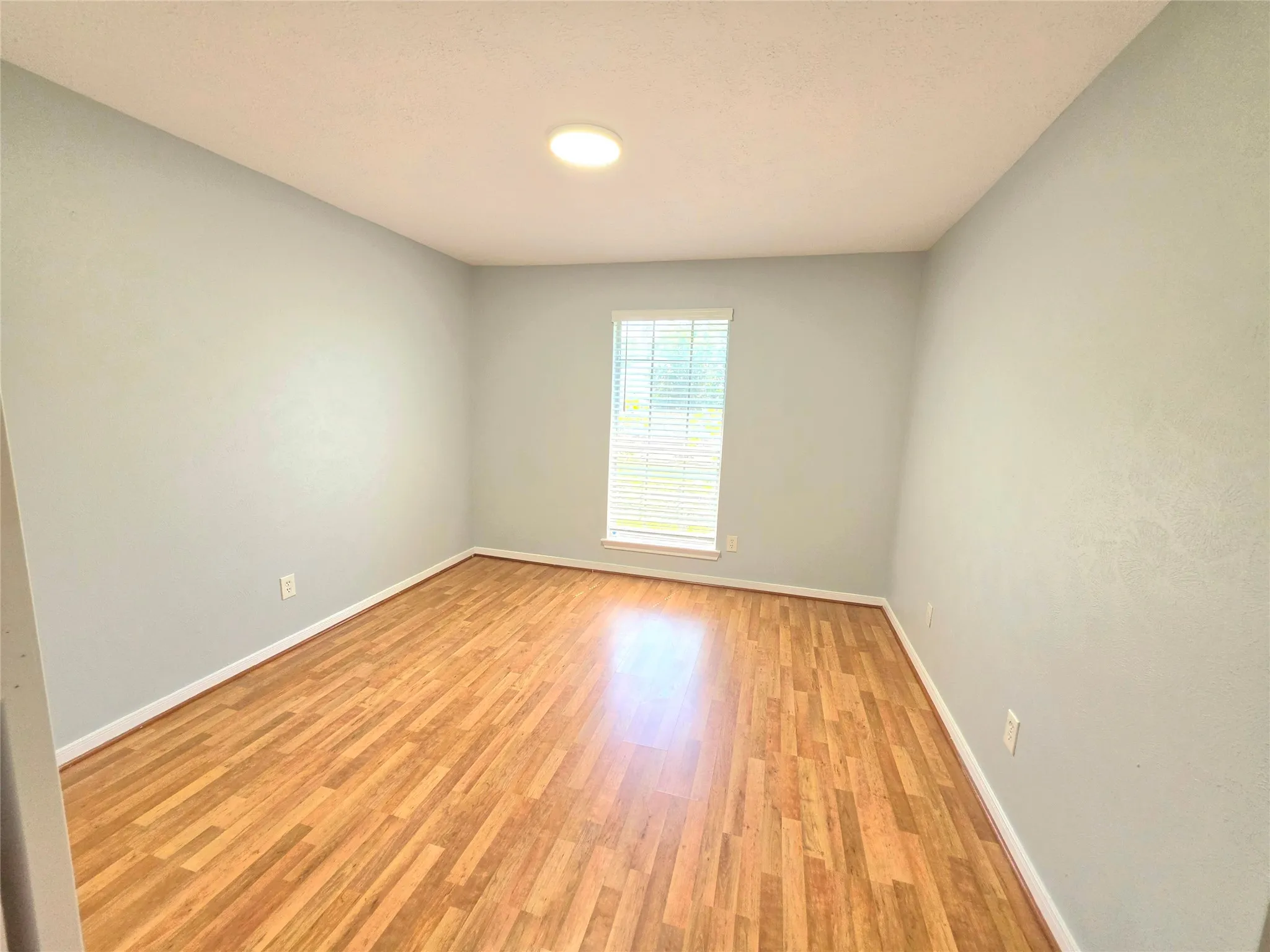 Room featuring wood-finish flooring, light-toned walls, and a window with blinds