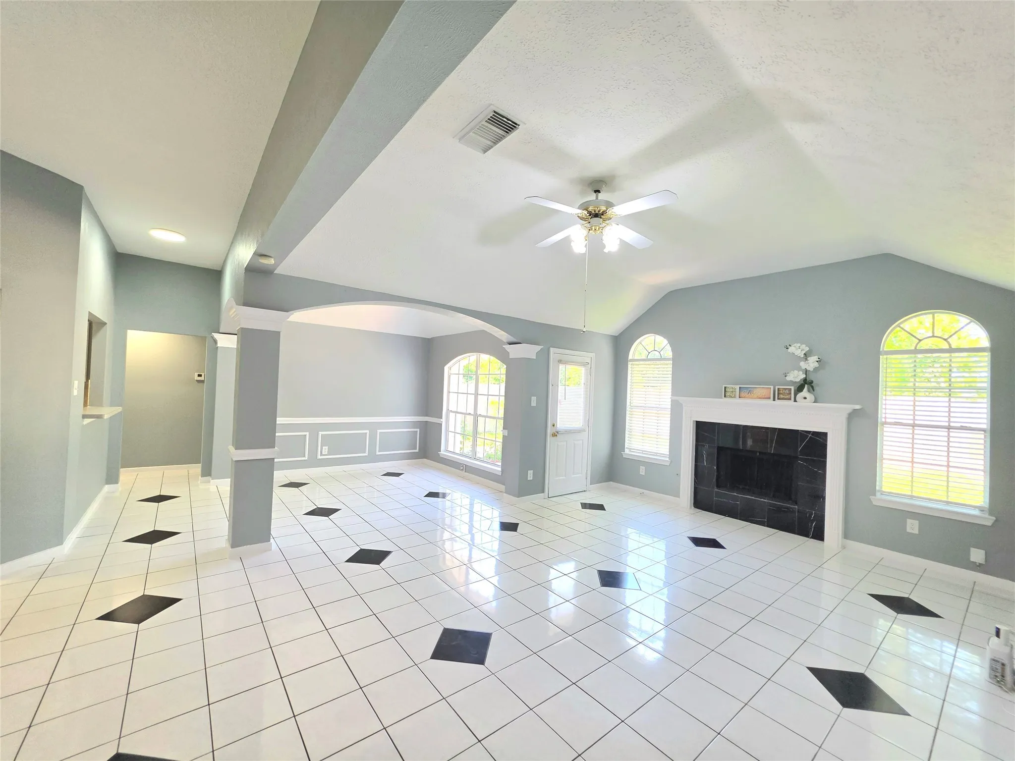 Spacious living area featuring white tile flooring with black diamond accents, a vaulted ceiling, and a ceiling fan