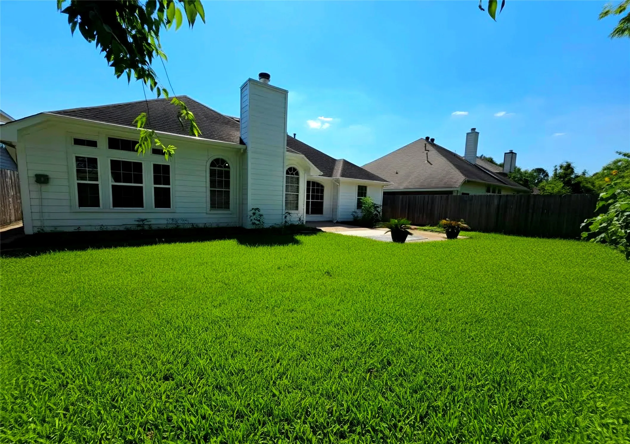 Expansive lawn area with a white residential structure featuring multiple windows, including arched designs, and a prominent chimney