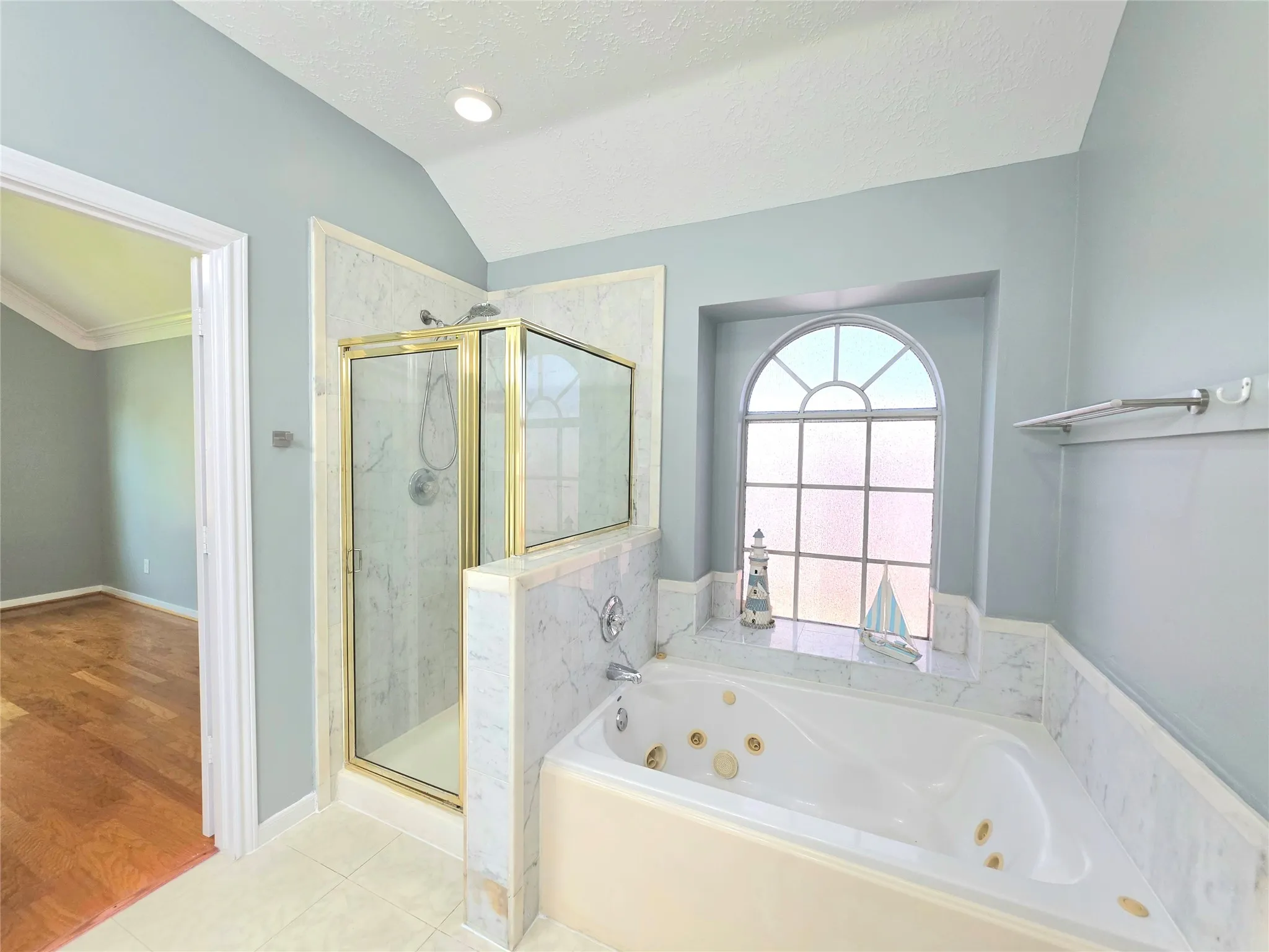 Soaking tub with jets, marble surround, and an arched window