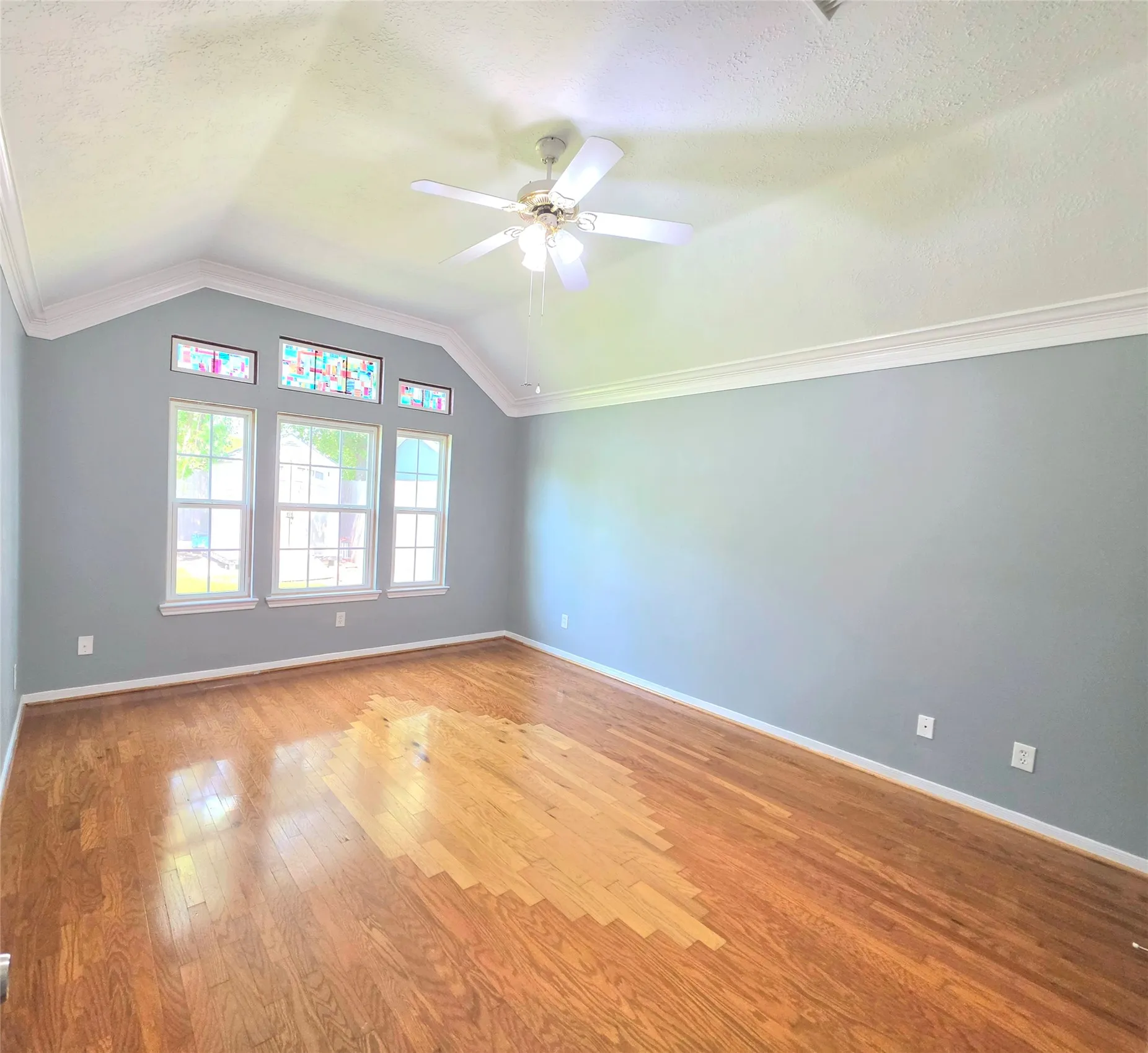 Vaulted ceiling room featuring wood-finish flooring, a ceiling fan, and crown molding