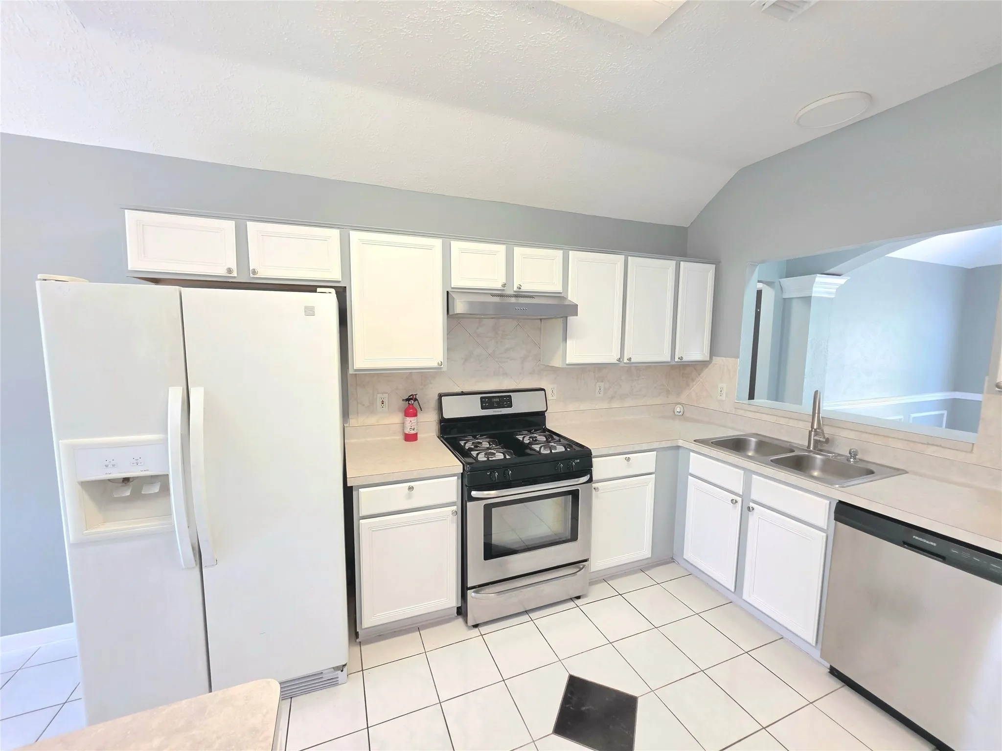 Kitchen featuring white cabinetry, light-toned countertops, a stainless steel gas range, and a double basin stainless steel sink