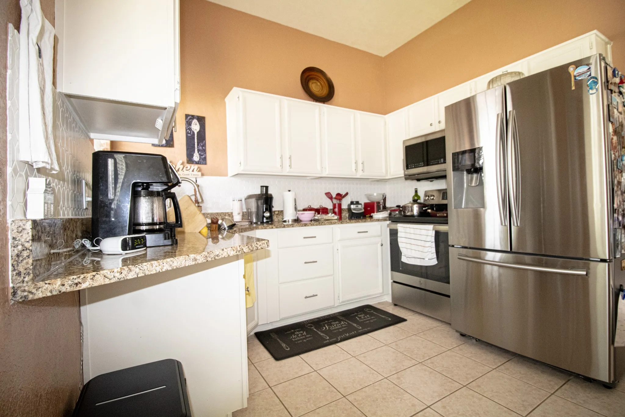 Kitchen with stainless steel appliances, white cabinetry, light tile patterned flooring, and granite counters