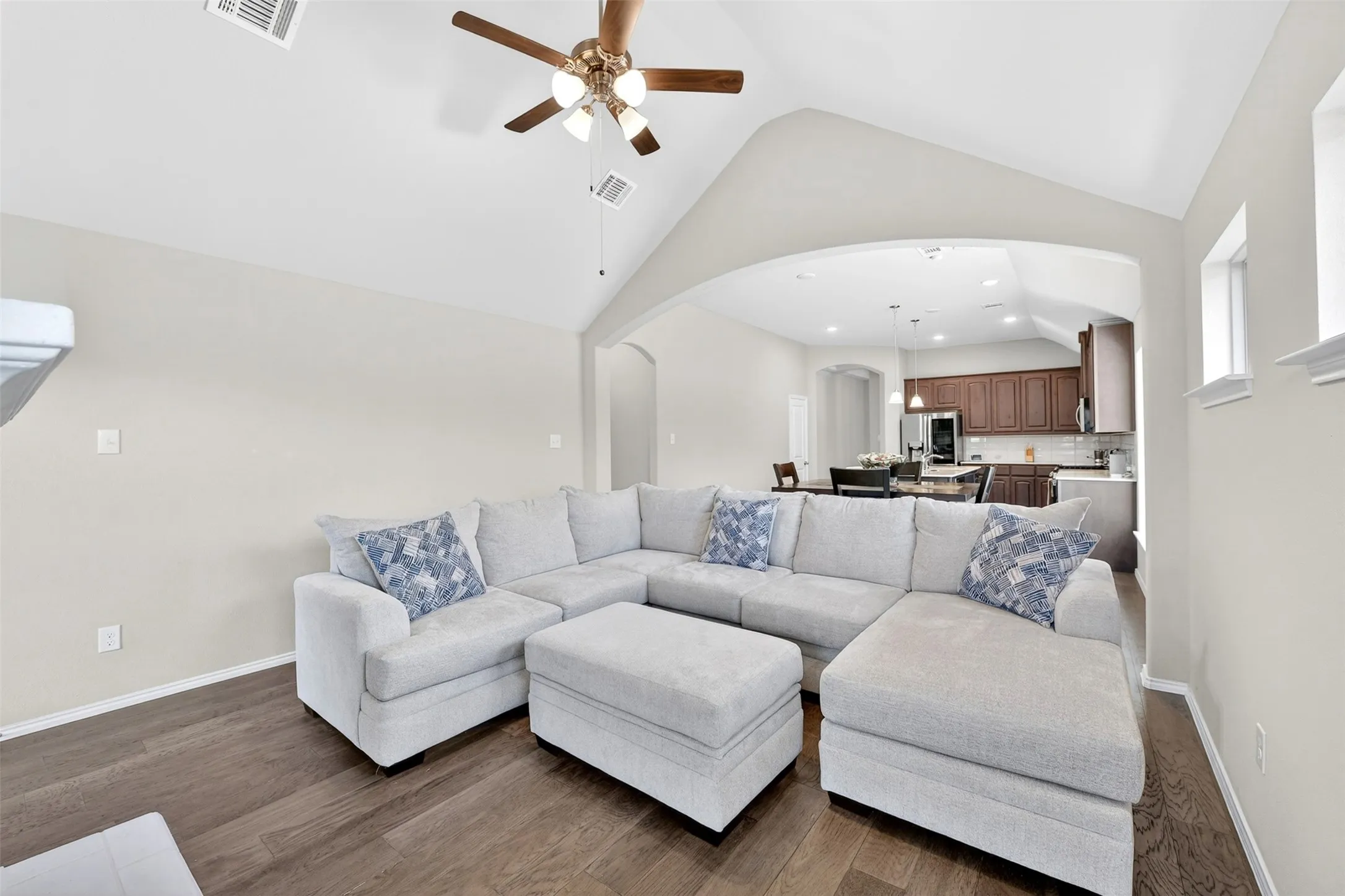 Living area featuring wood-finish flooring, vaulted ceilings with a ceiling fan, and an arched entryway to the kitchen