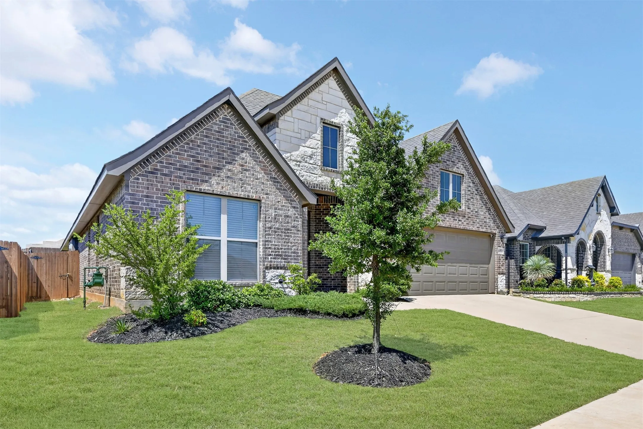 Contemporary residential exterior featuring a multi-textured facade with brick and stone accents, a gabled roofline, an attached garage, and a concrete driveway