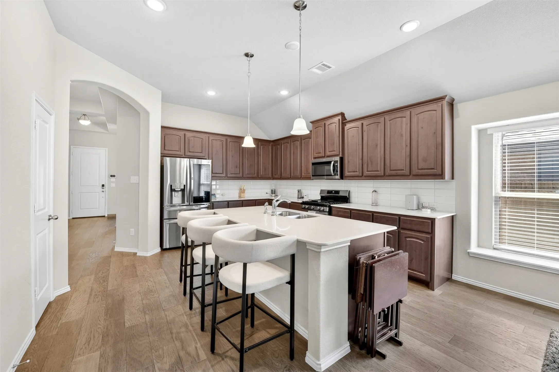 Kitchen featuring a central island with countertop seating, wood-finish flooring, dark wood cabinetry, stainless steel appliances, and a white subway tile backsplash