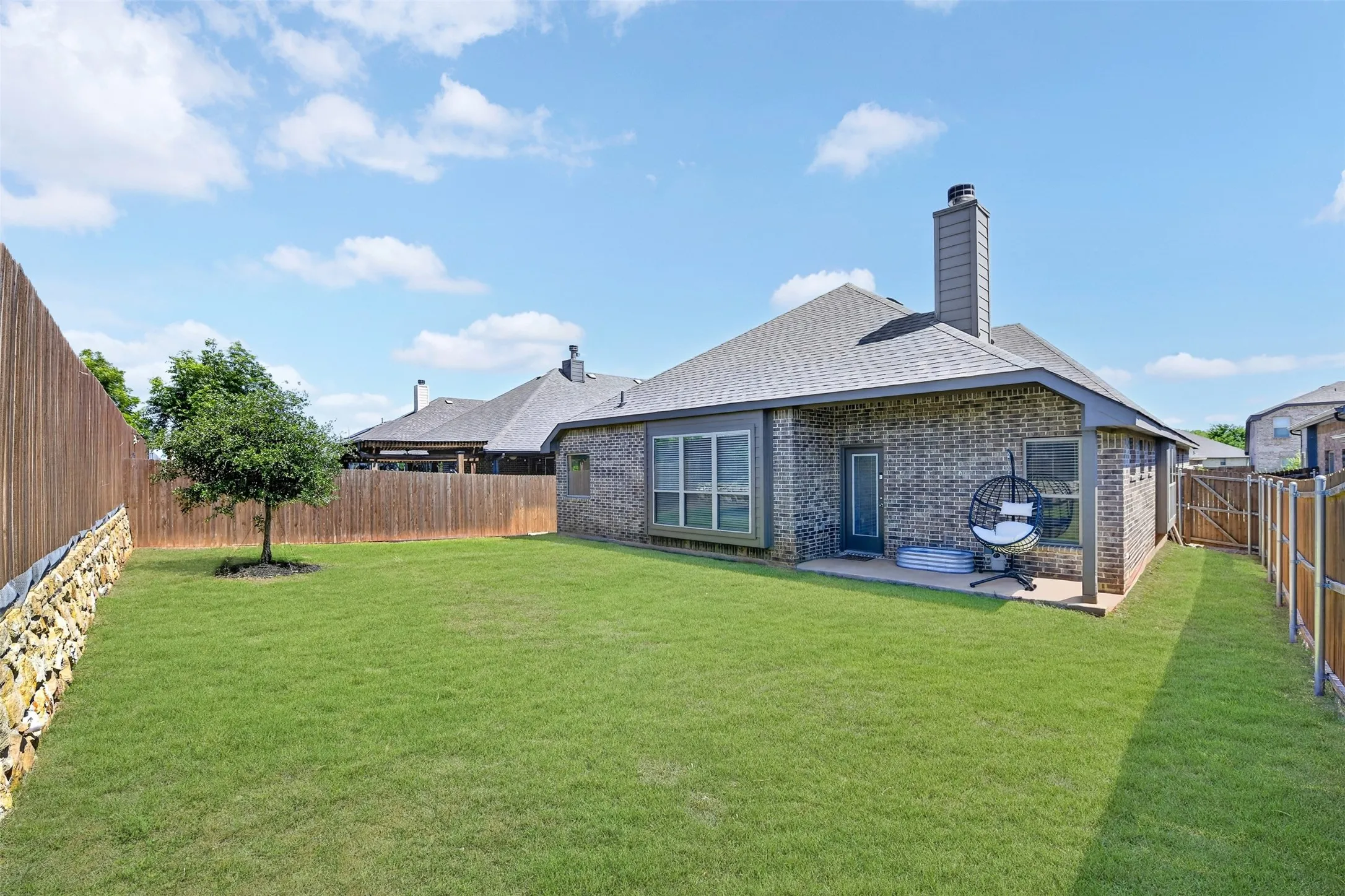 Spacious backyard featuring a brick exterior, covered patio, wood privacy fence, and a mature tree
