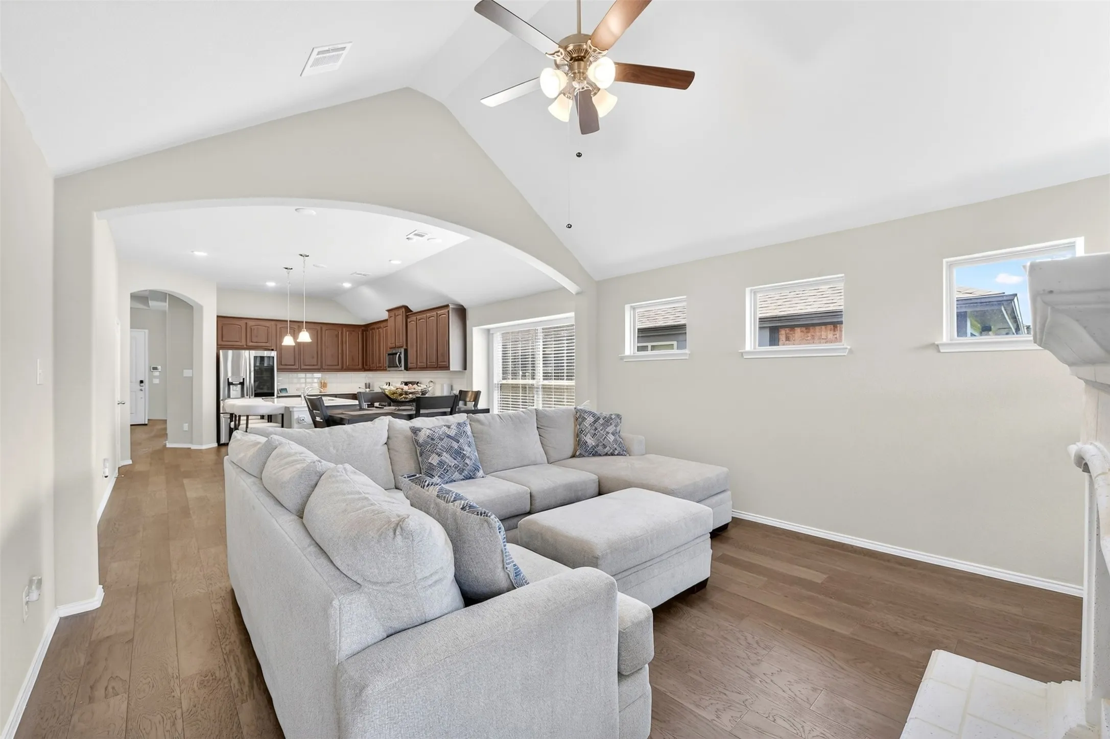 Living area featuring vaulted ceilings, wood-finish flooring, a ceiling fan, and multiple windows