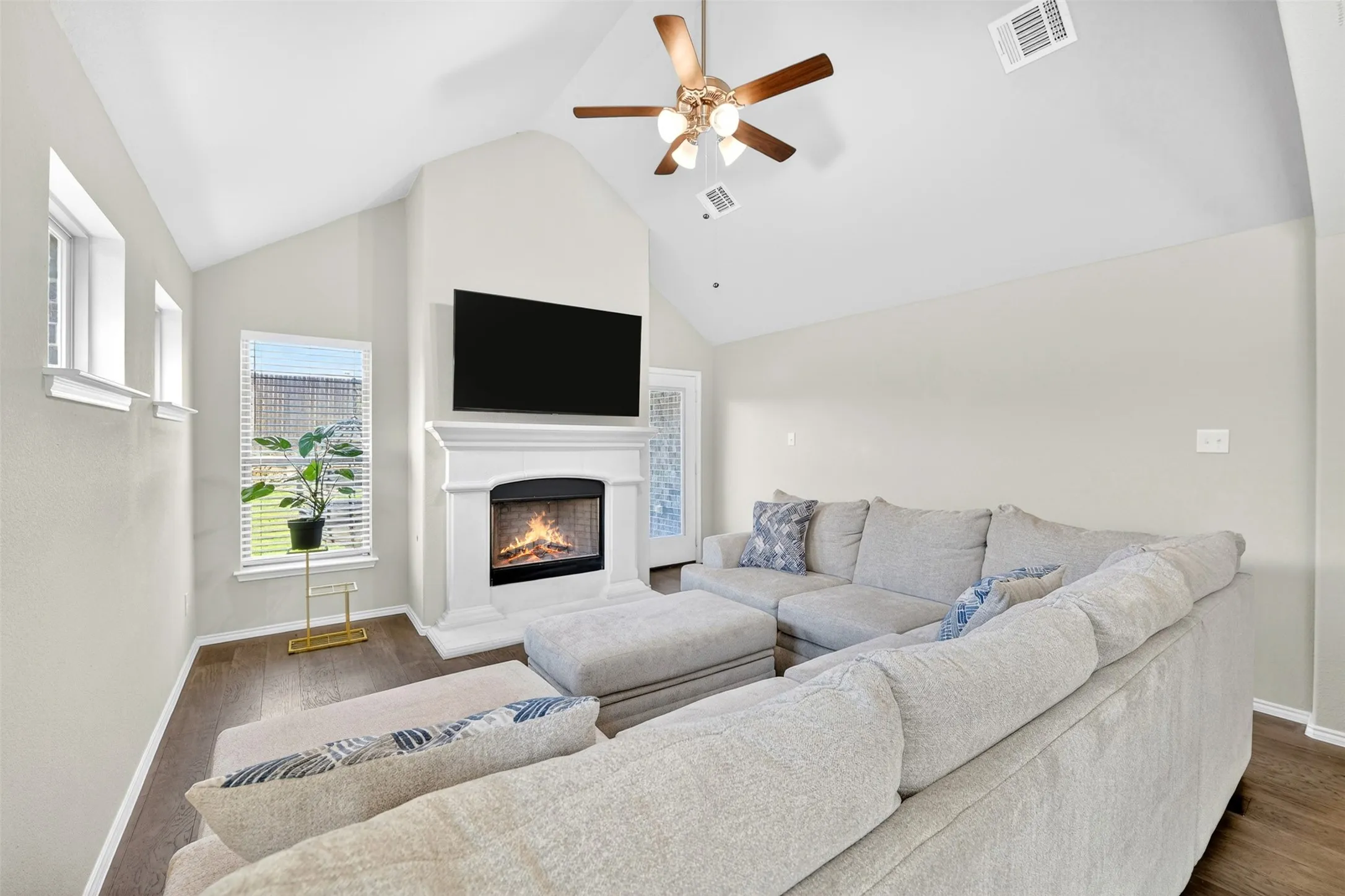Vaulted ceiling living area featuring wood-finish flooring, a white-mantled fireplace, and an integrated ceiling fan