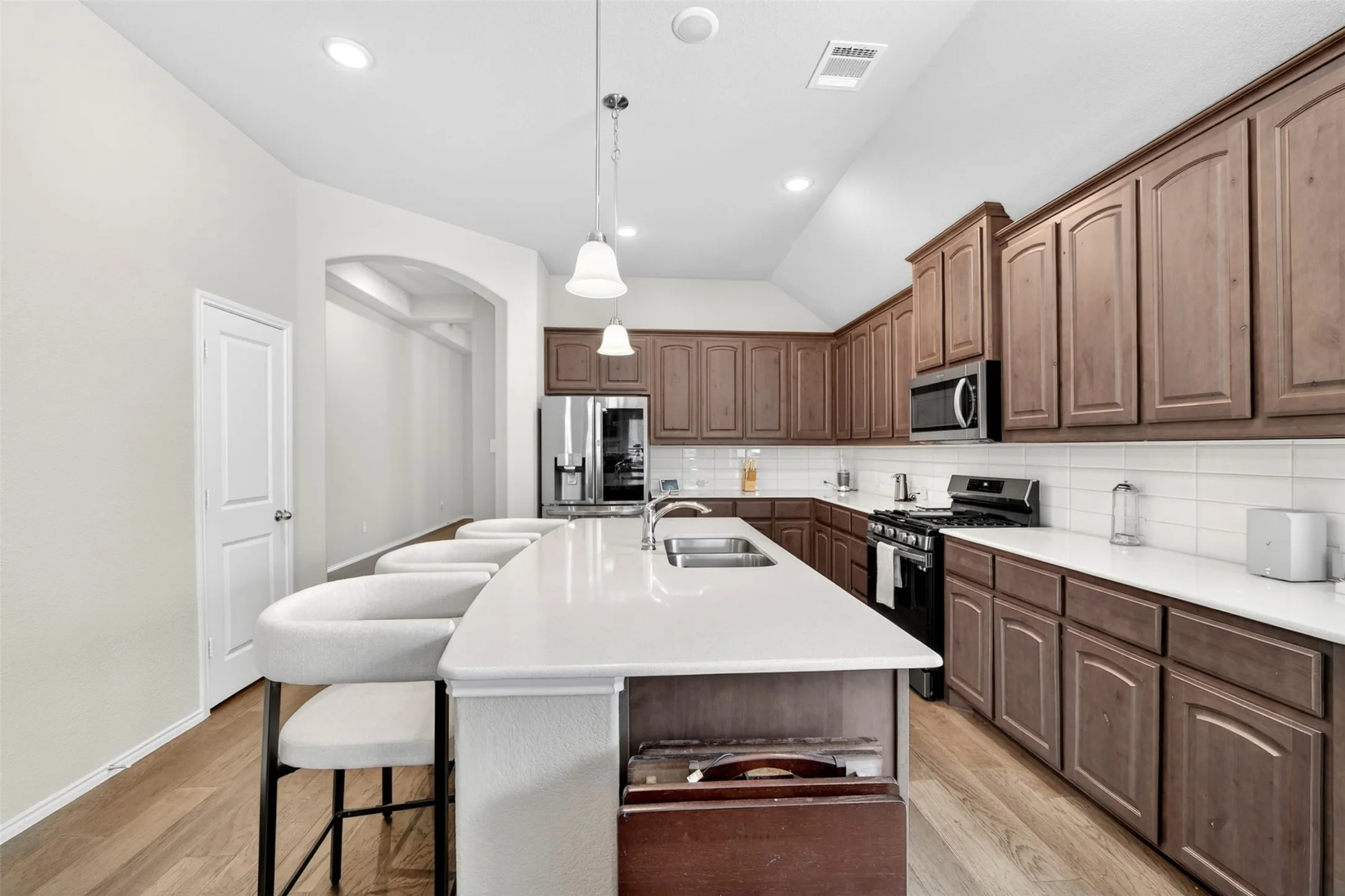 Kitchen featuring a spacious island with a double basin sink, stone-finish countertops, dark wood cabinetry, stainless steel appliances, and wood-finish flooring
