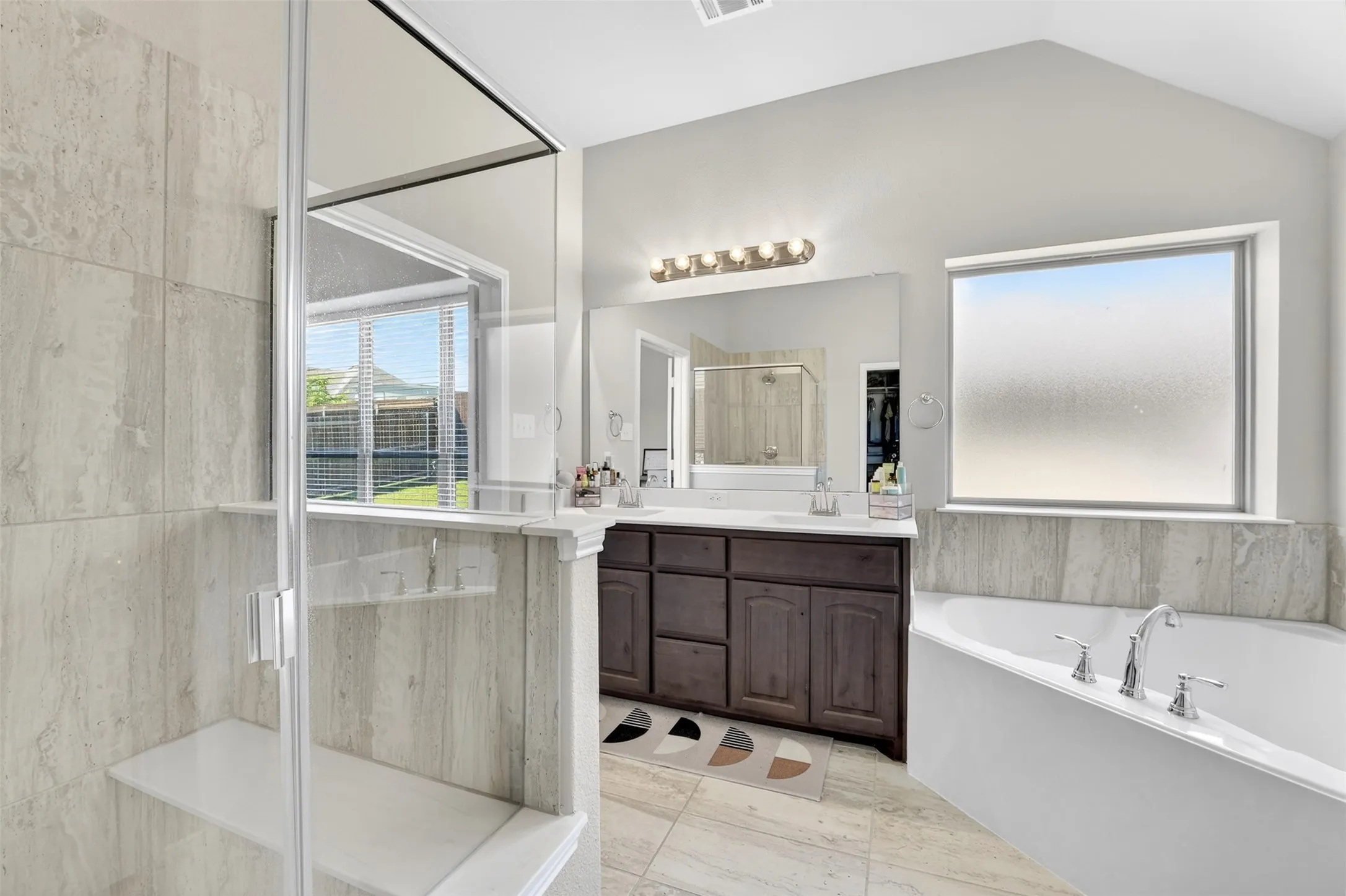 Spacious bathroom featuring a glass-enclosed shower with integrated bench, a separate soaking tub, and a dual vanity with ample storage