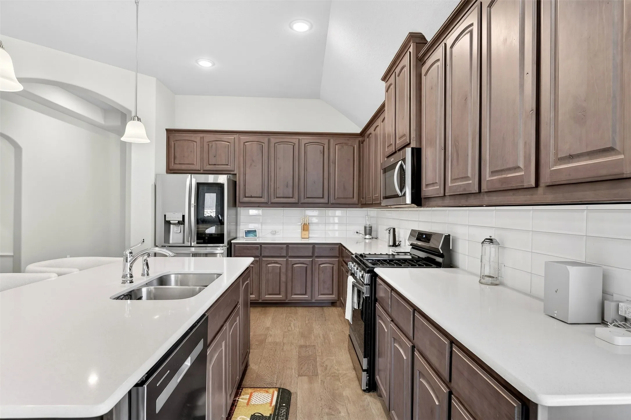 Modern kitchen featuring extensive wood cabinetry, white countertops, stainless steel appliances, a double basin sink, and wood-finish flooring