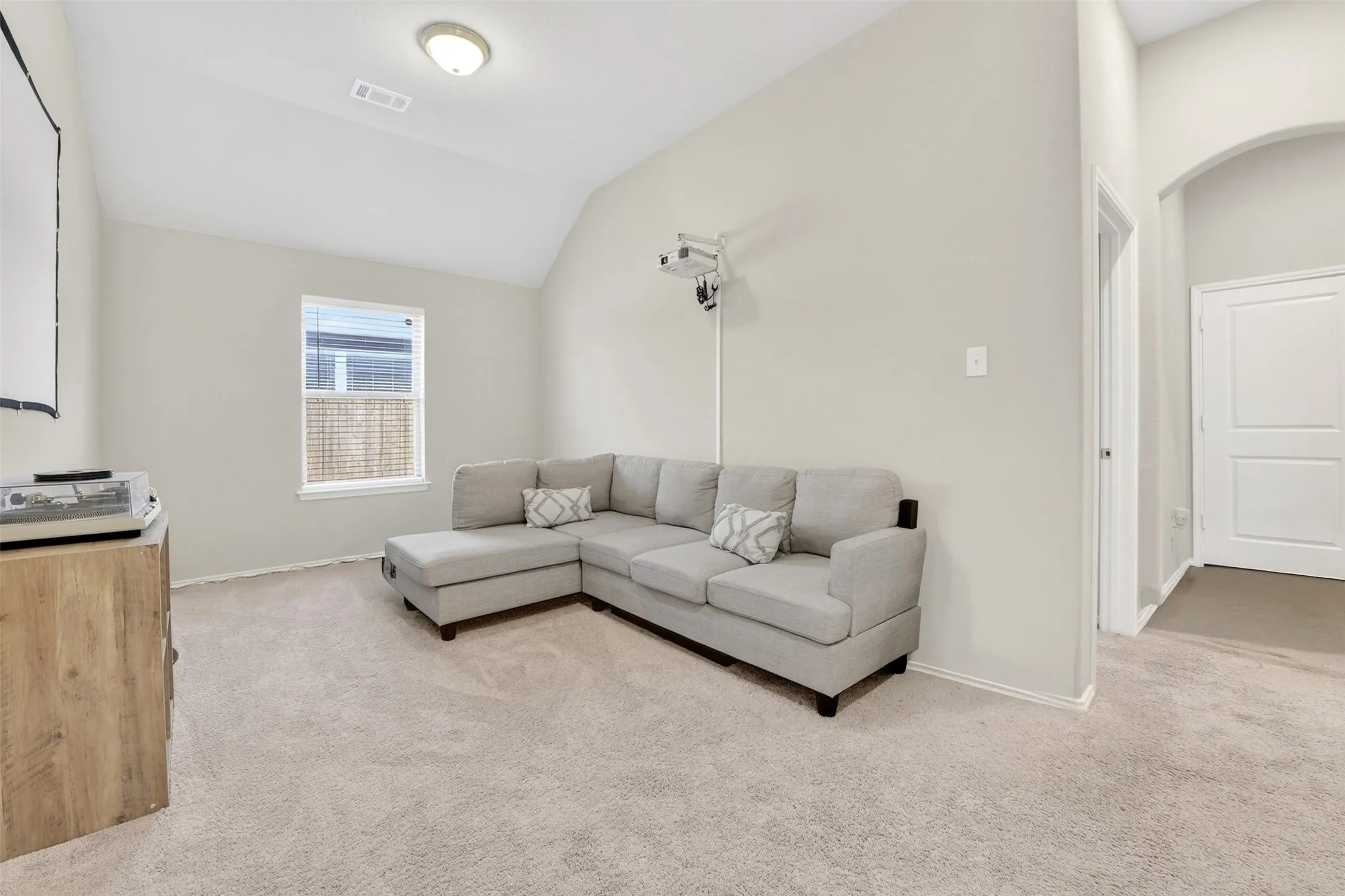 Carpeted room featuring a single window with blinds, a vaulted ceiling, and an arched doorway