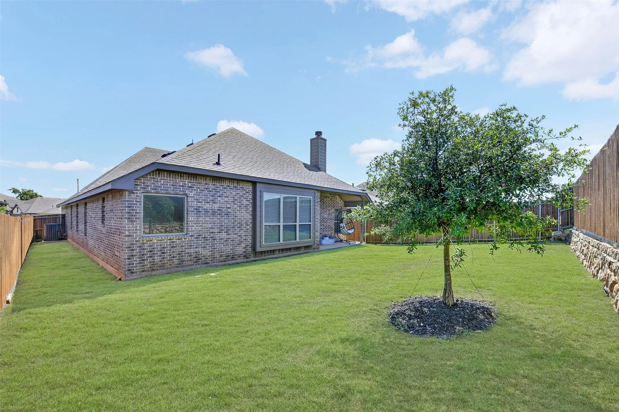 Expansive green lawn with a young tree, bordered by a wood privacy fence