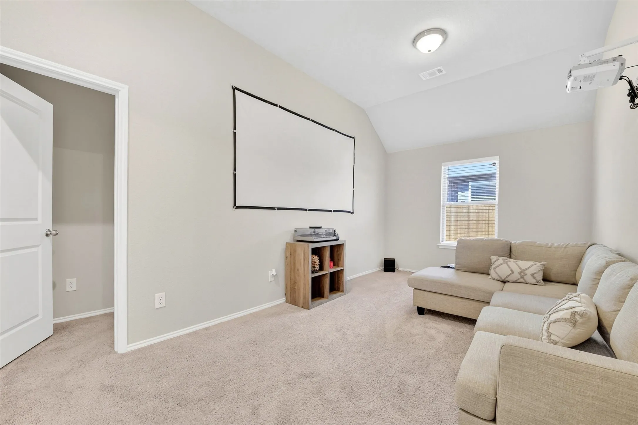 Carpeted room featuring a ceiling-mounted projector, wall-mounted screen, and a single window with blinds