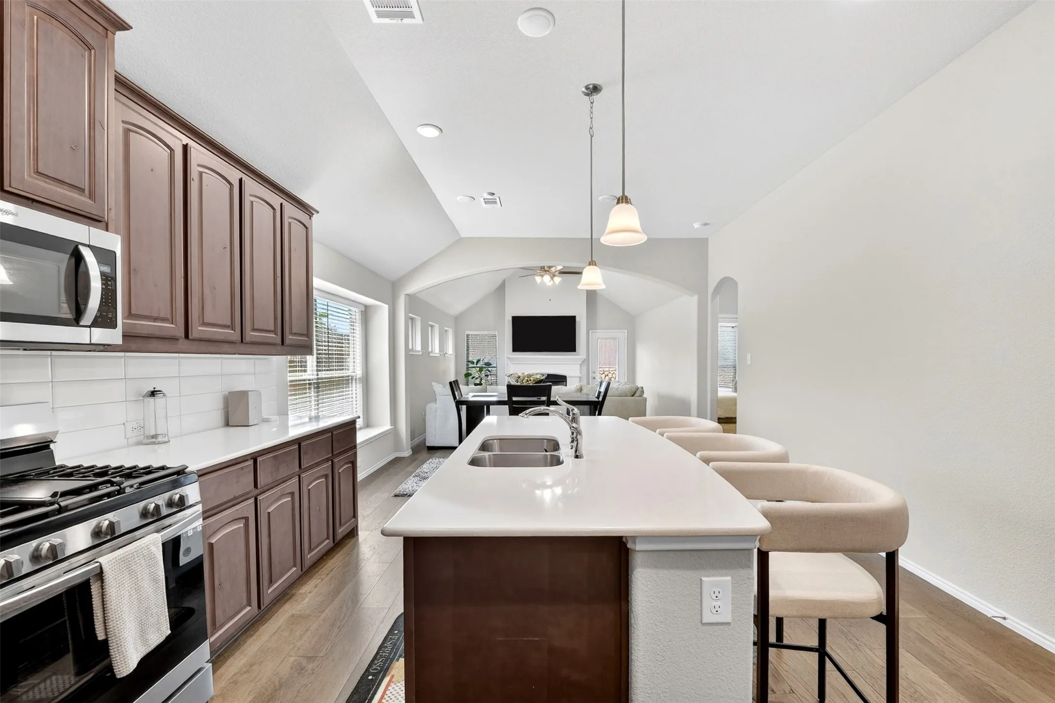 Kitchen featuring a spacious island with dual sinks, pendant lighting, stainless steel appliances, wood-finish flooring, and white countertops