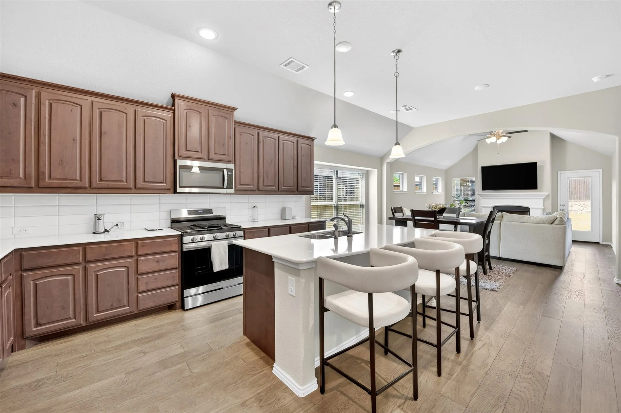 Open-concept kitchen featuring wood-finish flooring, white subway tile backsplash, and stainless steel appliances
