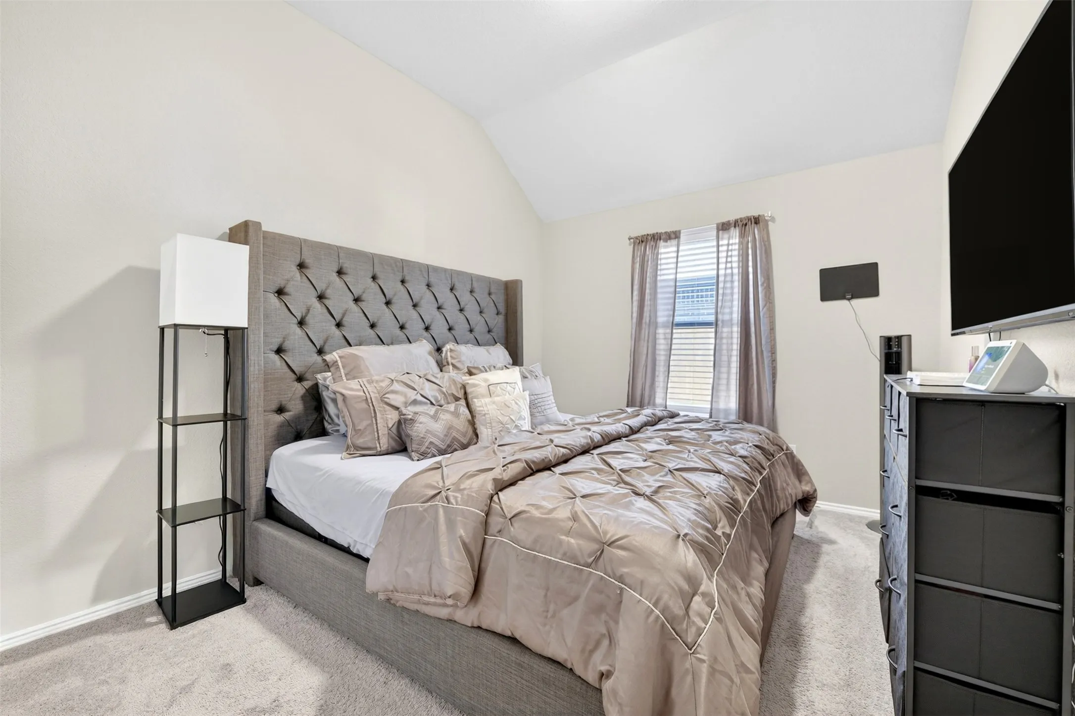 Carpeted interior space featuring a vaulted ceiling and a window with blinds and drapes