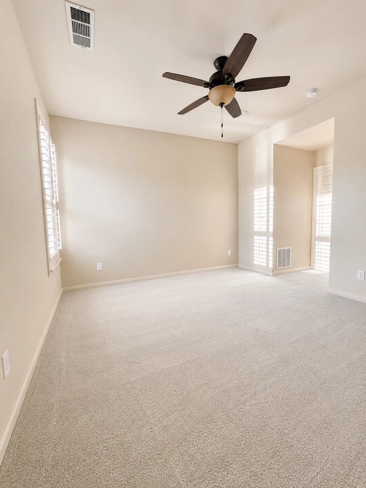 3rd bedroom upstairs is an expansive freshly carpeted room featuring a ceiling fan with integrated lighting, multiple windows with white plantation shutters, and newly painted, light-toned walls