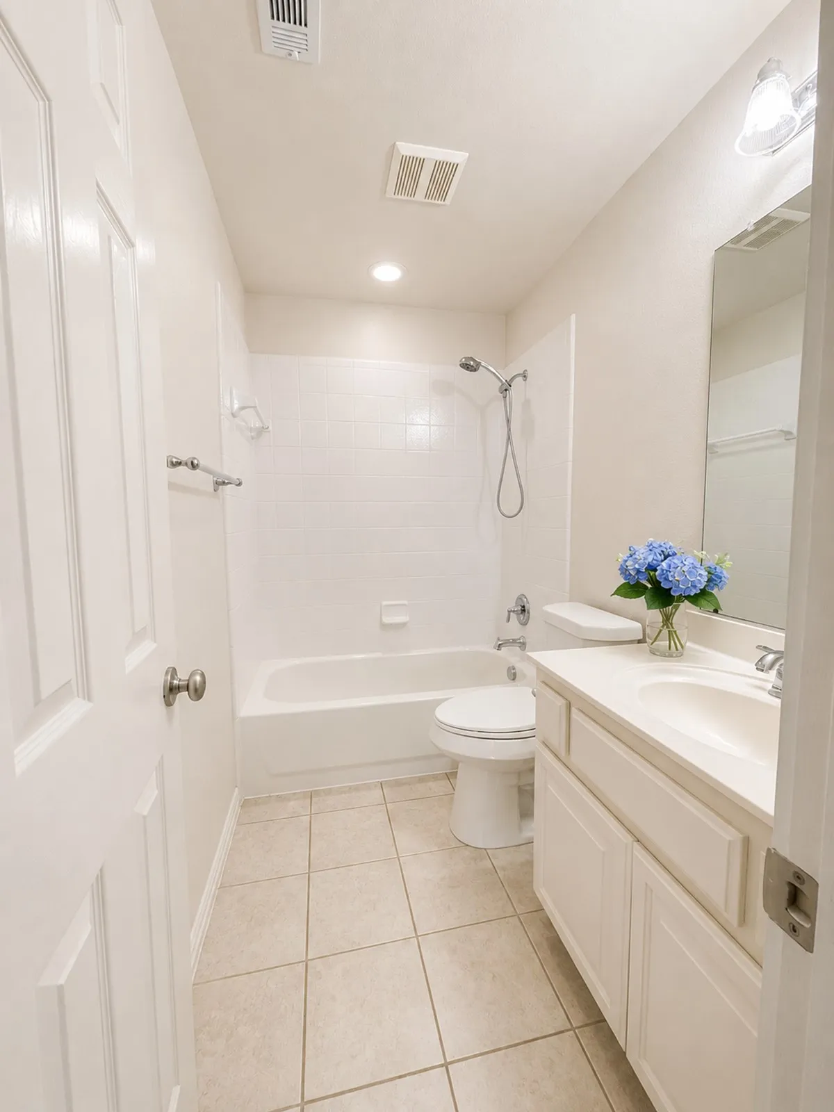 Bathroom featuring a white vanity with integrated sink, a full-size bathtub with subway tile surround, a toilet, and neutral-toned floor tiling