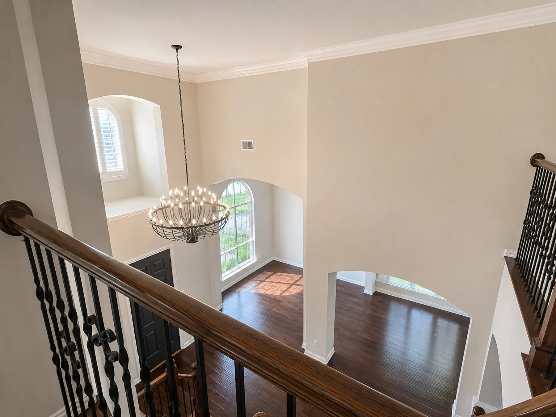Two-story foyer featuring a prominent chandelier, dark wood-finish flooring, arched doorways, and a decorative wrought iron staircase railing with a wood handrail