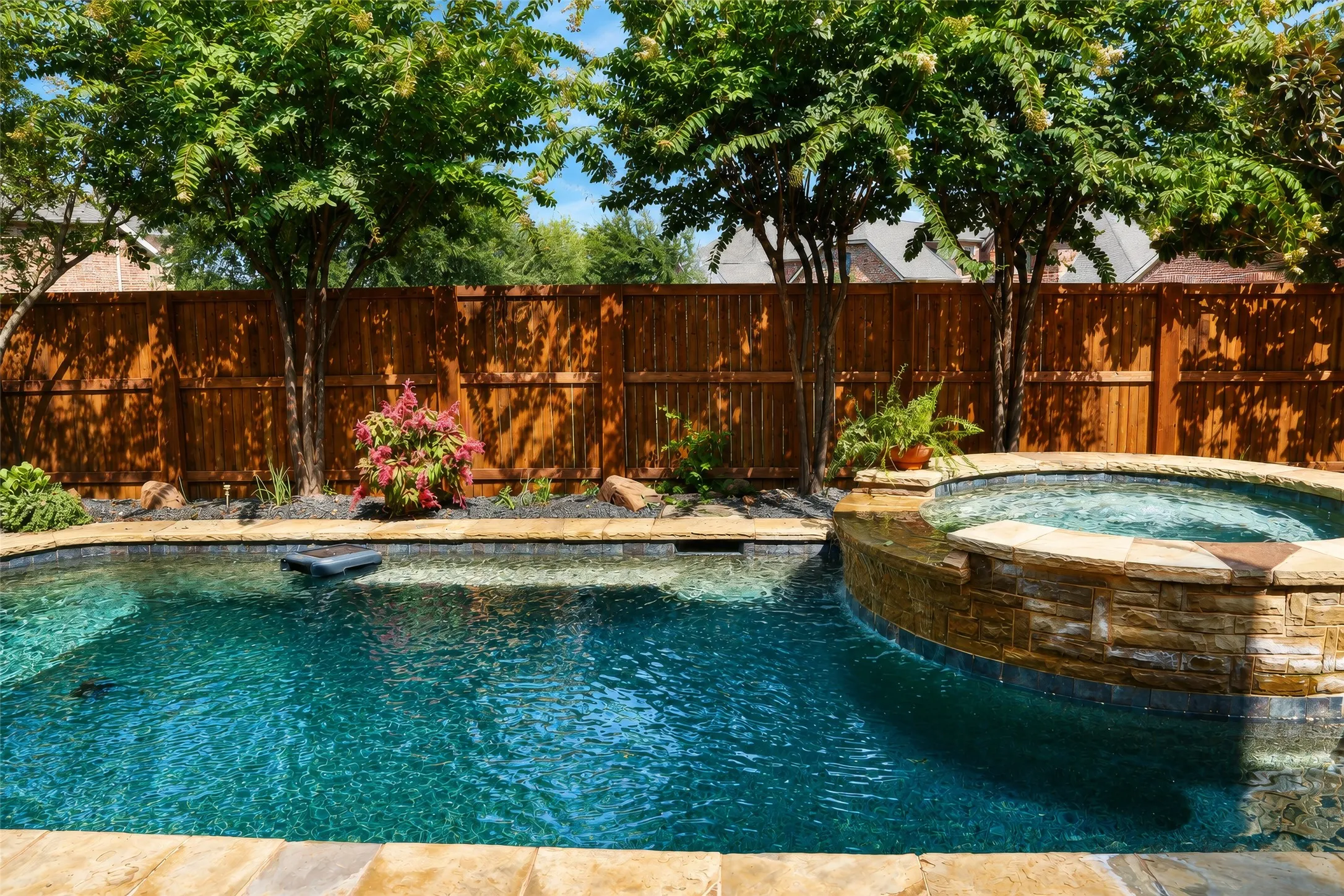 In-ground swimming pool featuring a built-in spa with stone-finish surround, natural stone coping, and a privacy fence