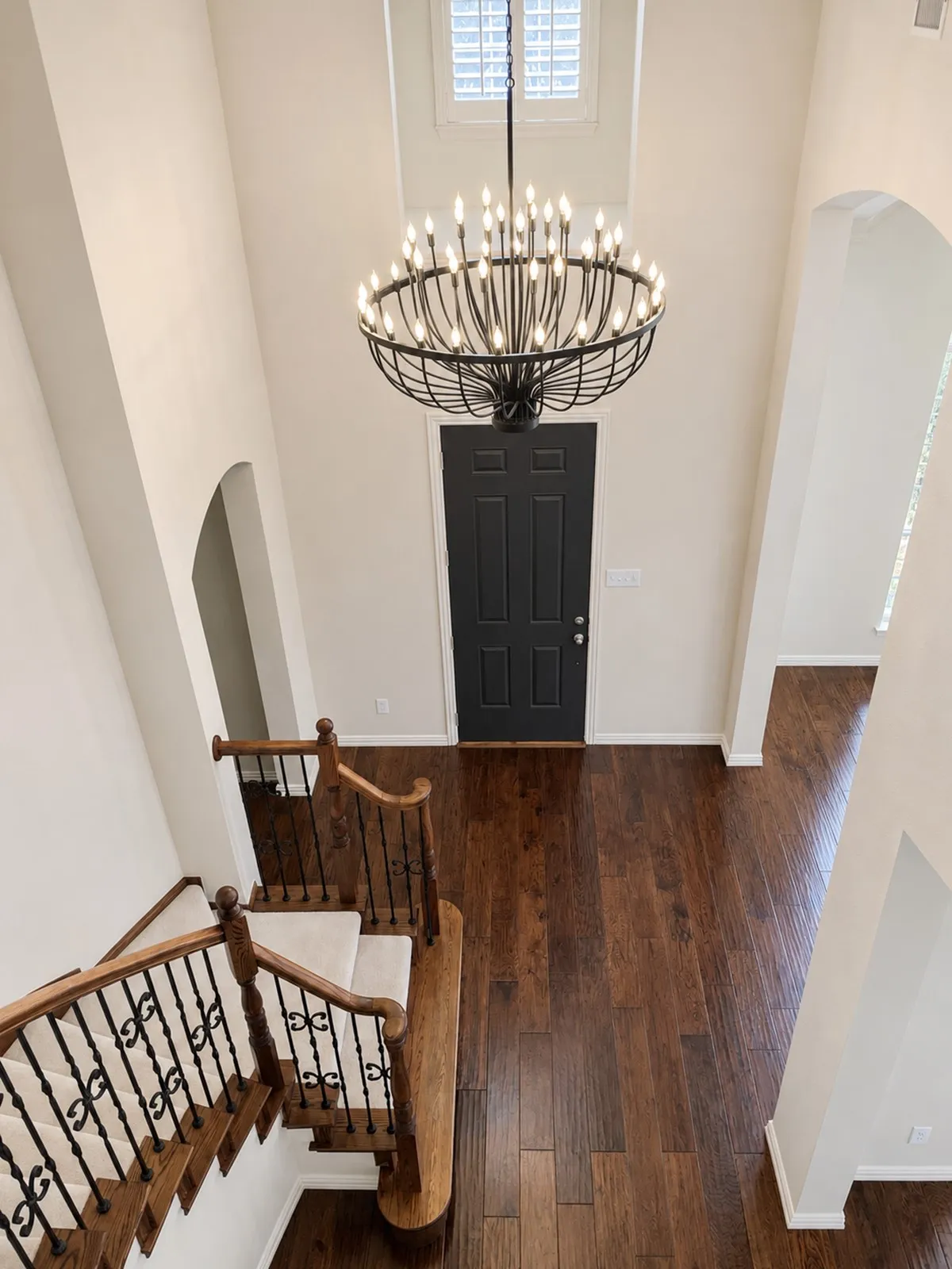 Two-story foyer featuring dark wood-finish flooring, a grand staircase with wrought iron balusters and carpeted treads, and a new gorgeous multi-tiered chandelier