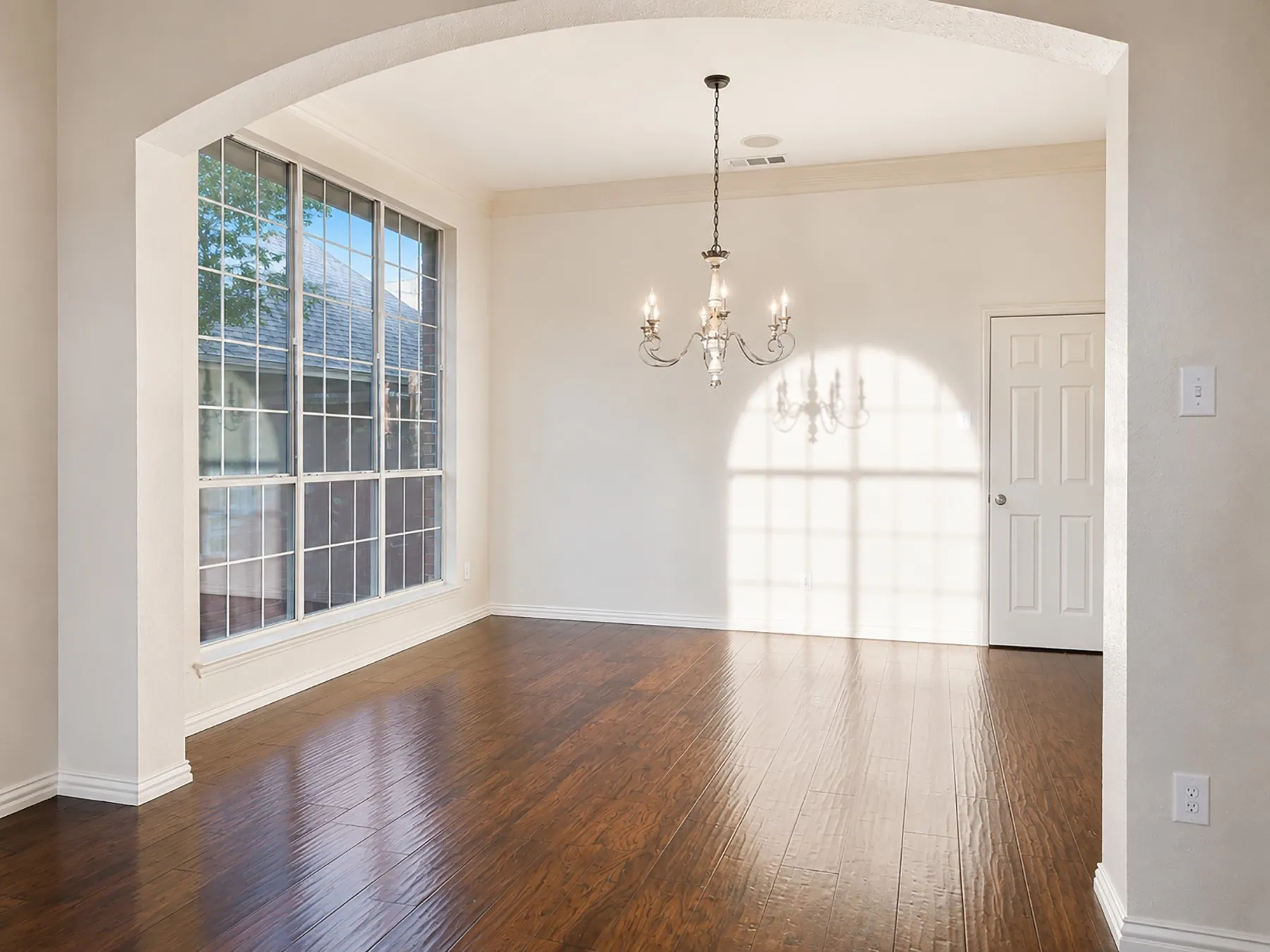 Spacious room featuring wood-finish flooring, a large window with grid pattern, and an ornate chandelier