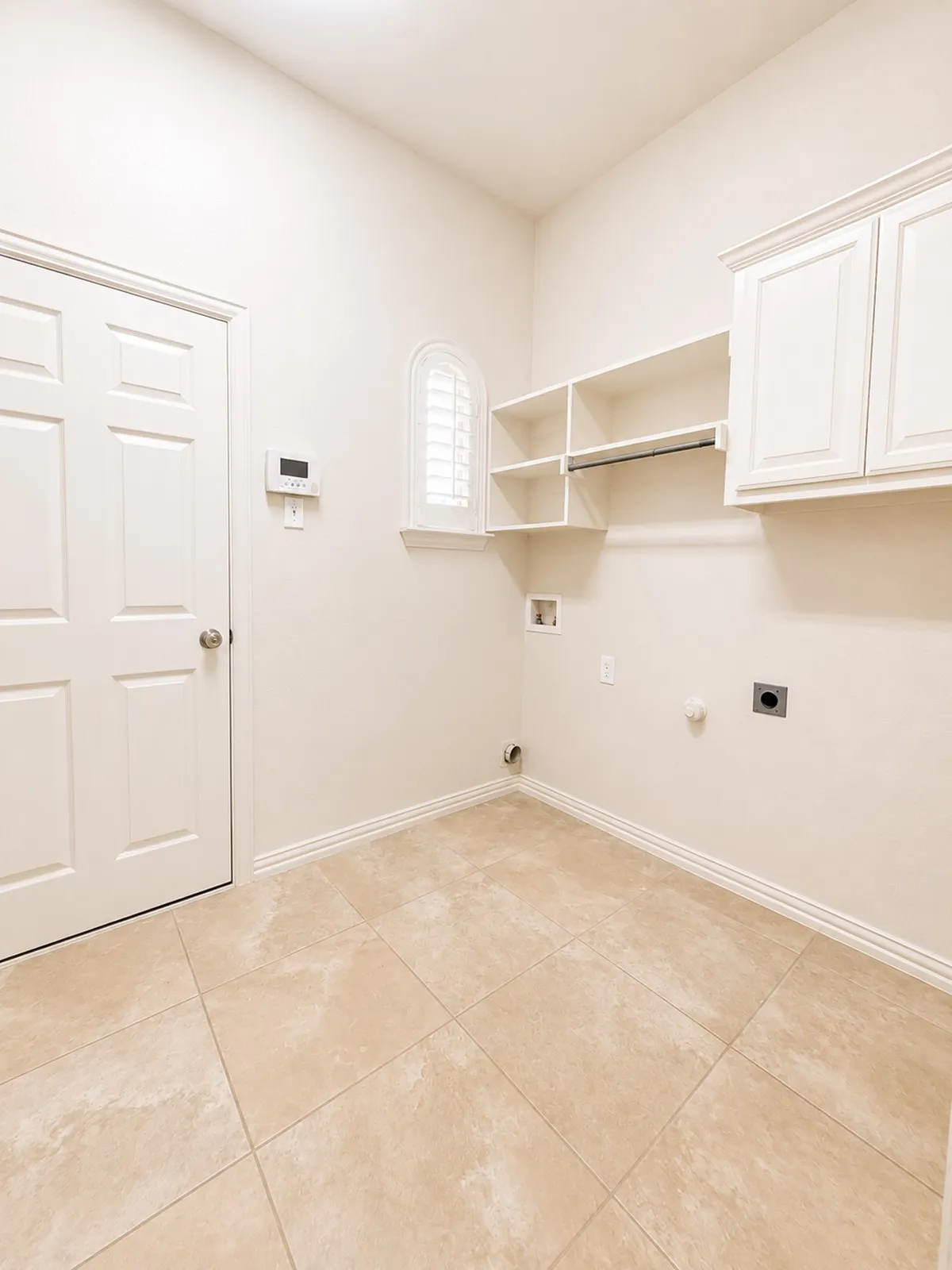 Utility space featuring large-format ceramic tile flooring and light-toned walls with ample storage space.
