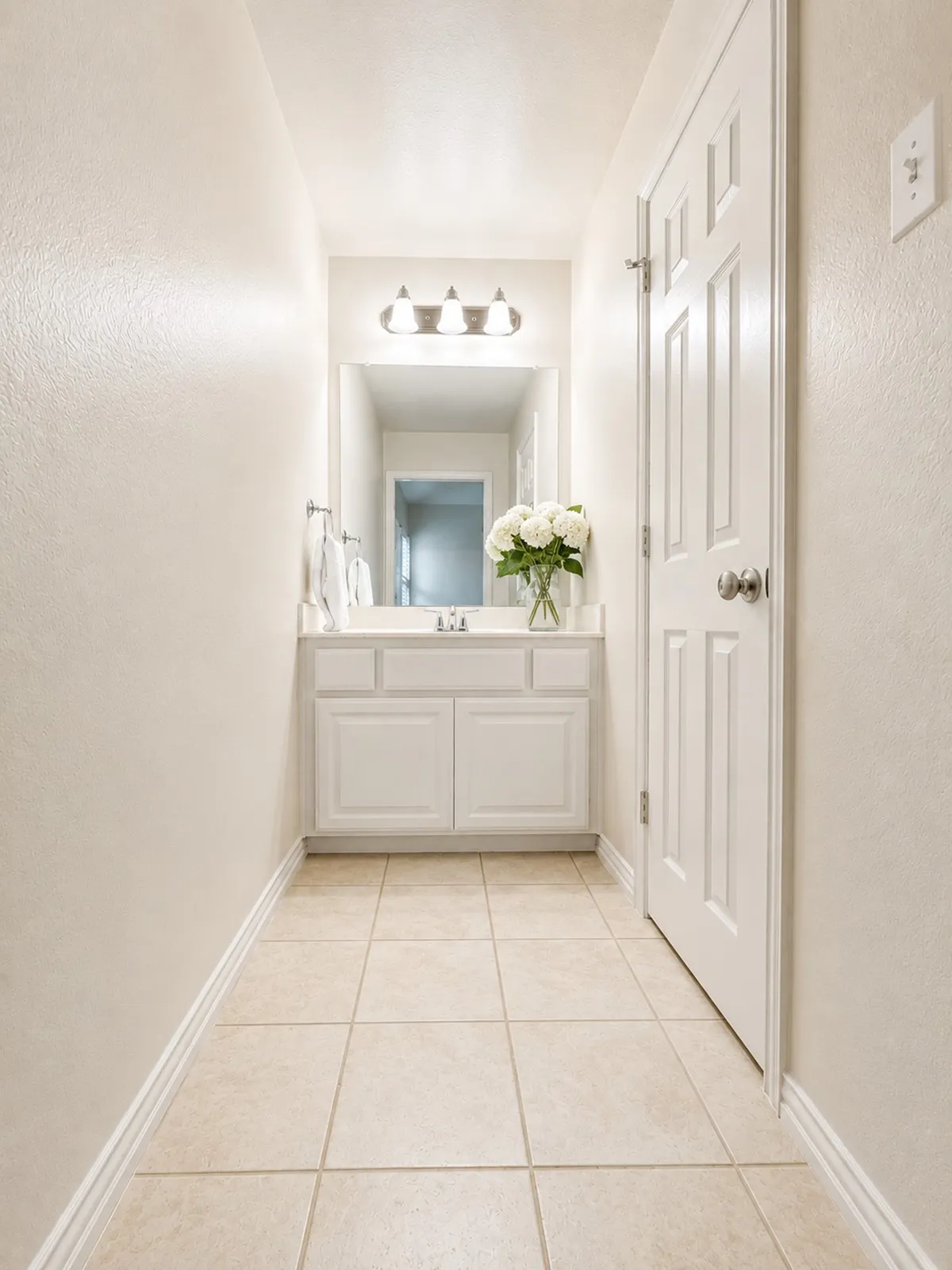 Jack and Jill vanity area featuring a rectangular mirror, three-light fixture, white cabinetry with silver-tone hardware, and a single basin sink