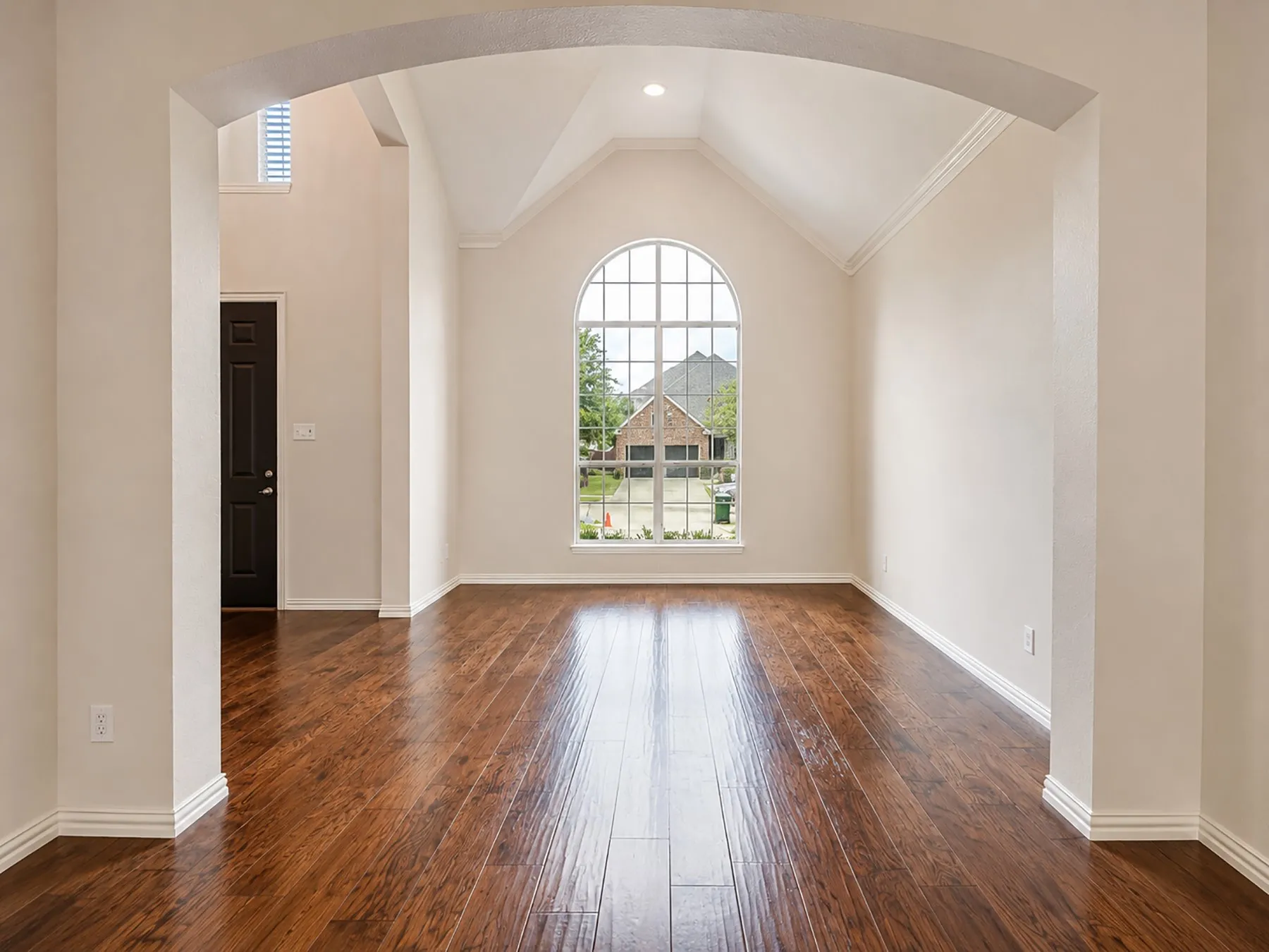 Archway entry to a room featuring high vaulted ceilings, a large arched window with grid pattern, beautiful flooring, and crisp white baseboards