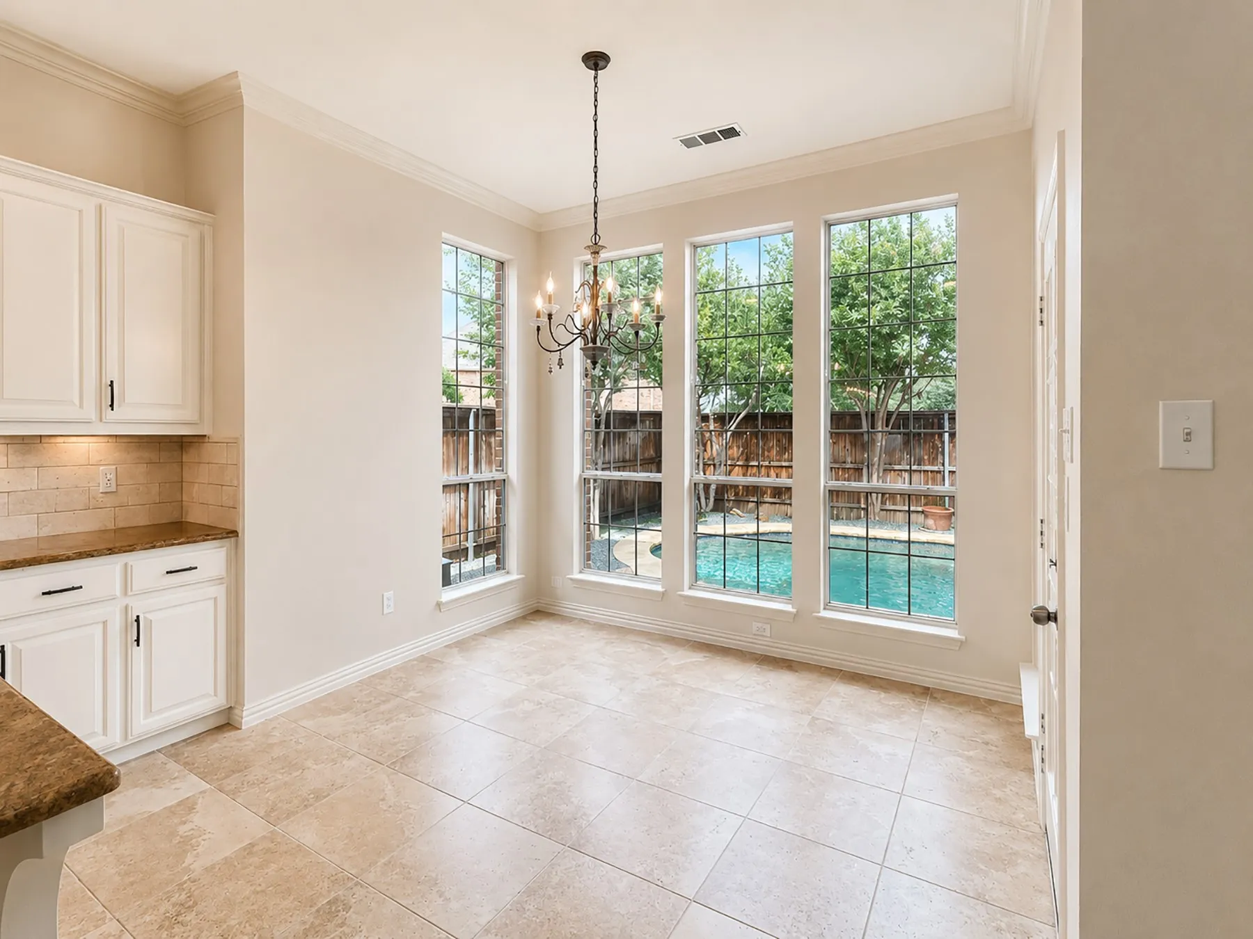 Breakfast nook featuring three large windows overlooking a backyard pool, a traditional chandelier, tile flooring, and crown molding