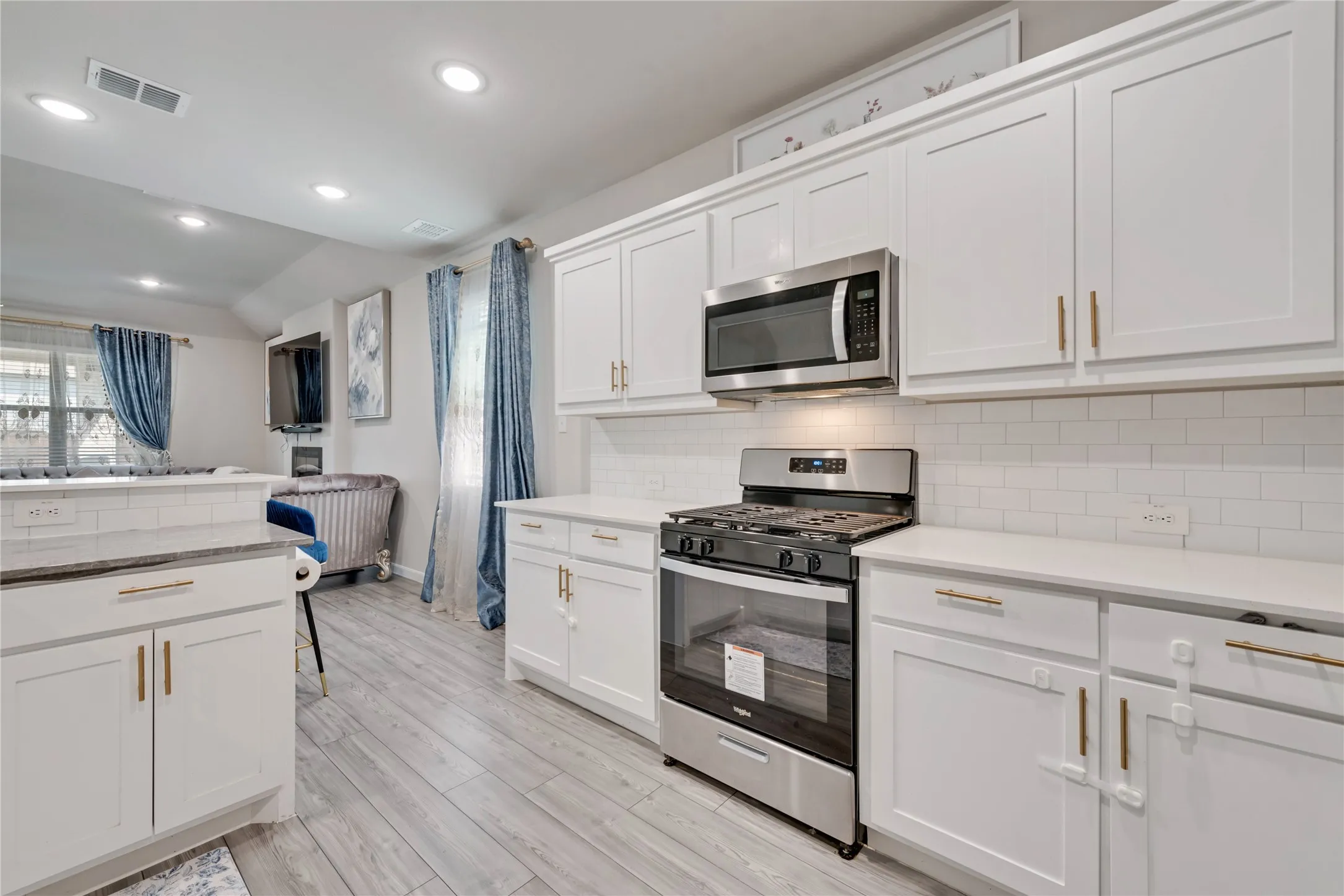 Kitchen with light wood-style floors, white cabinets, visible vents, appliances with stainless steel finishes, and decorative backsplash