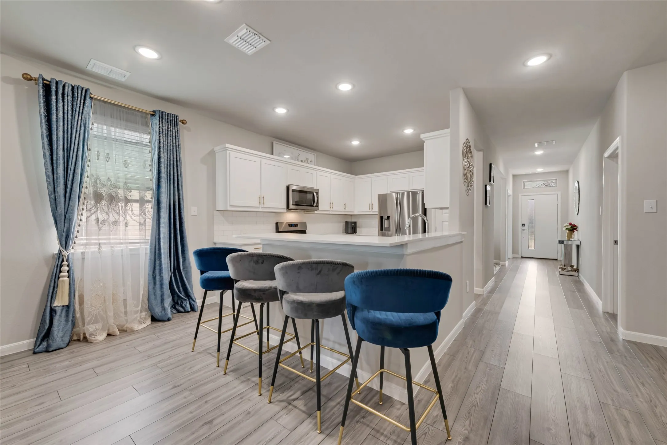Kitchen with visible vents, light wood-type flooring, appliances with stainless steel finishes, and a kitchen bar