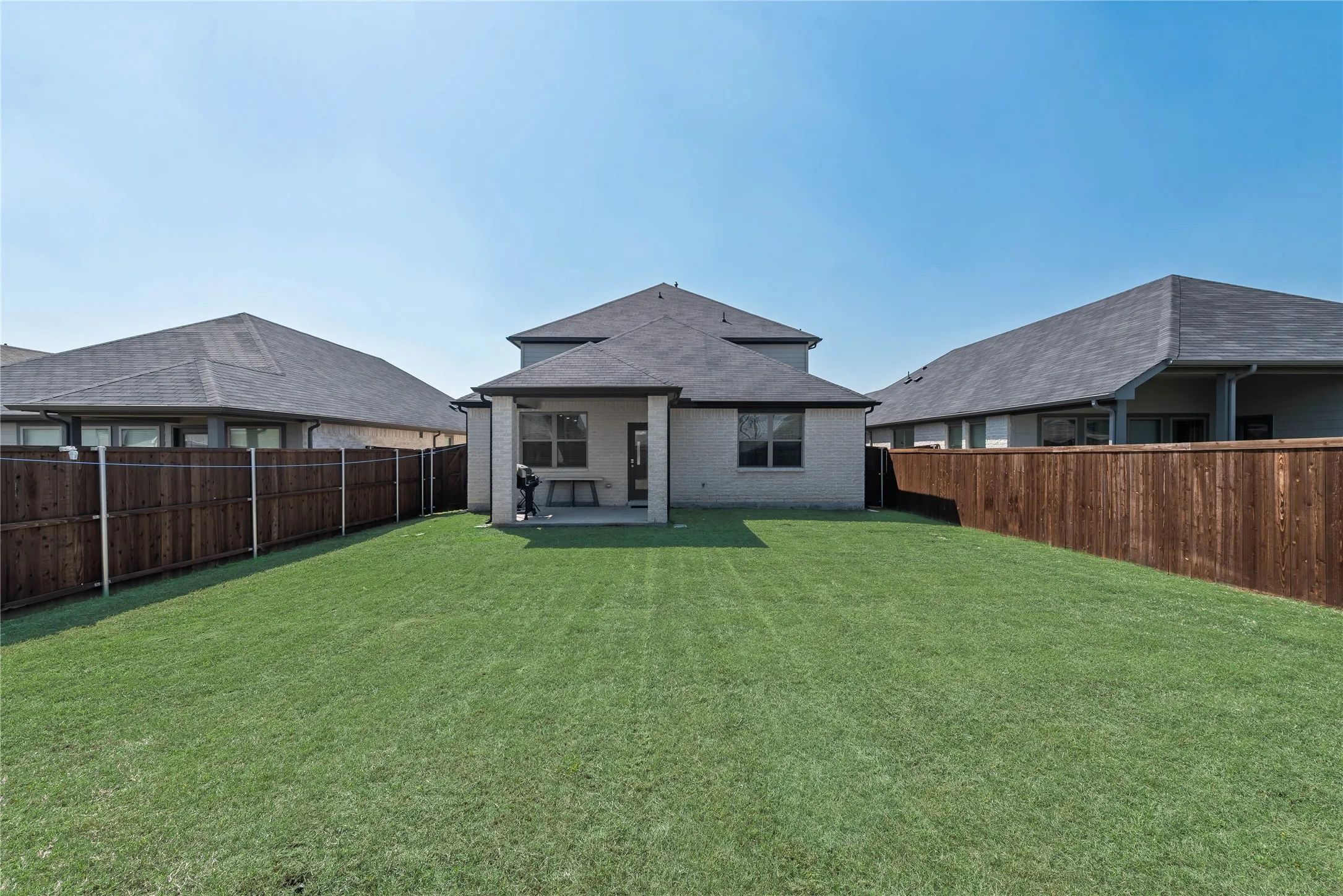 Rear view of property with a yard, brick siding, a fenced backyard, and a patio area