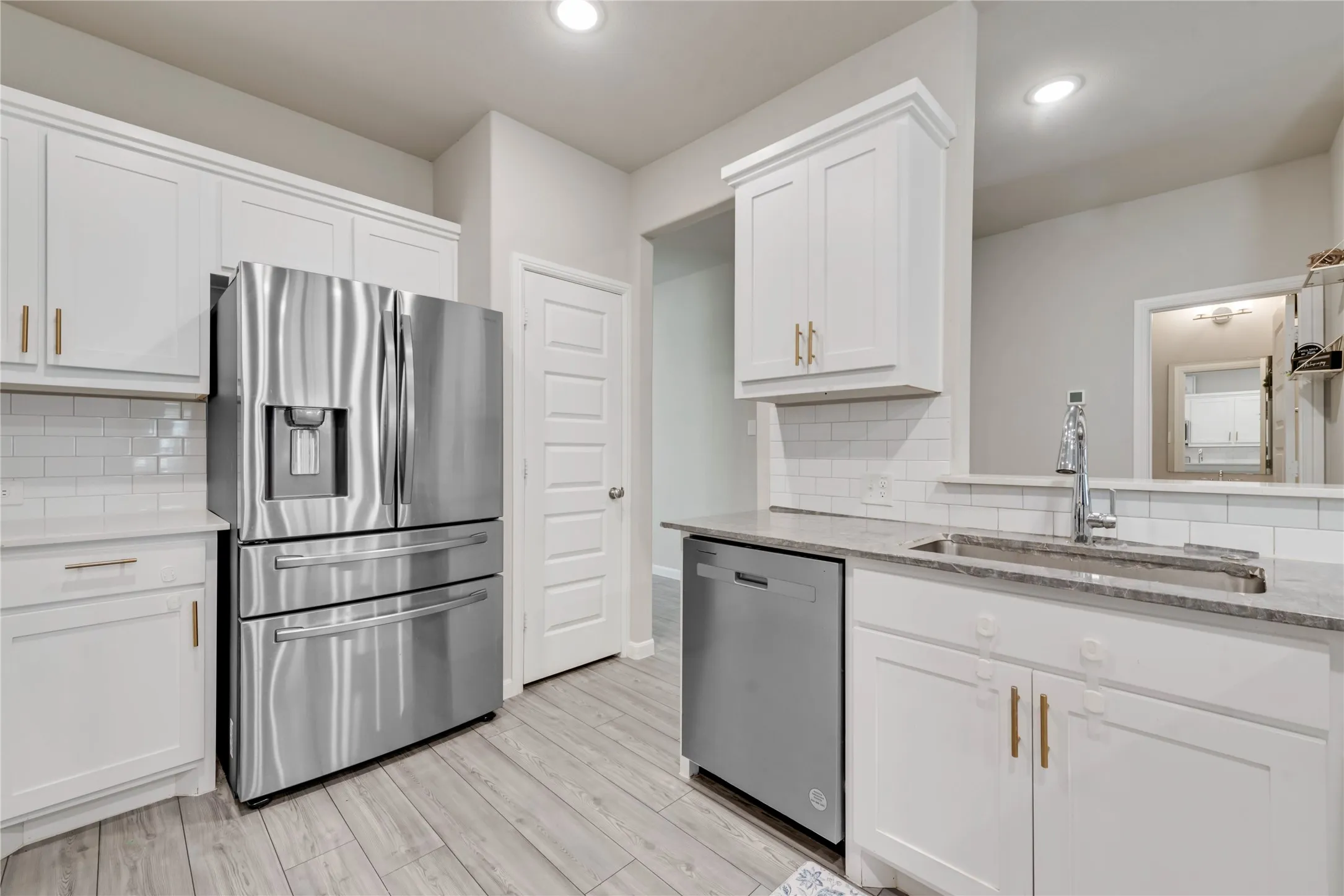 Kitchen with white cabinets, a sink, appliances with stainless steel finishes, light wood finished floors, and backsplash