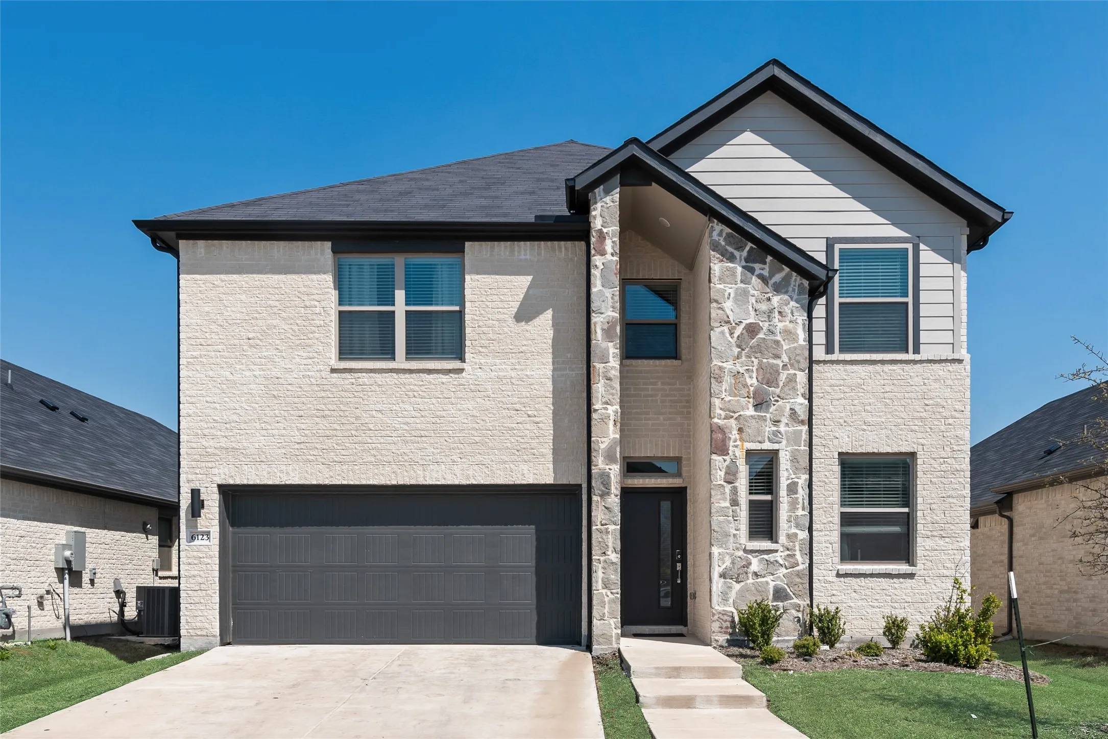 View of front facade featuring concrete driveway, central AC unit, stone siding, and an attached garage
