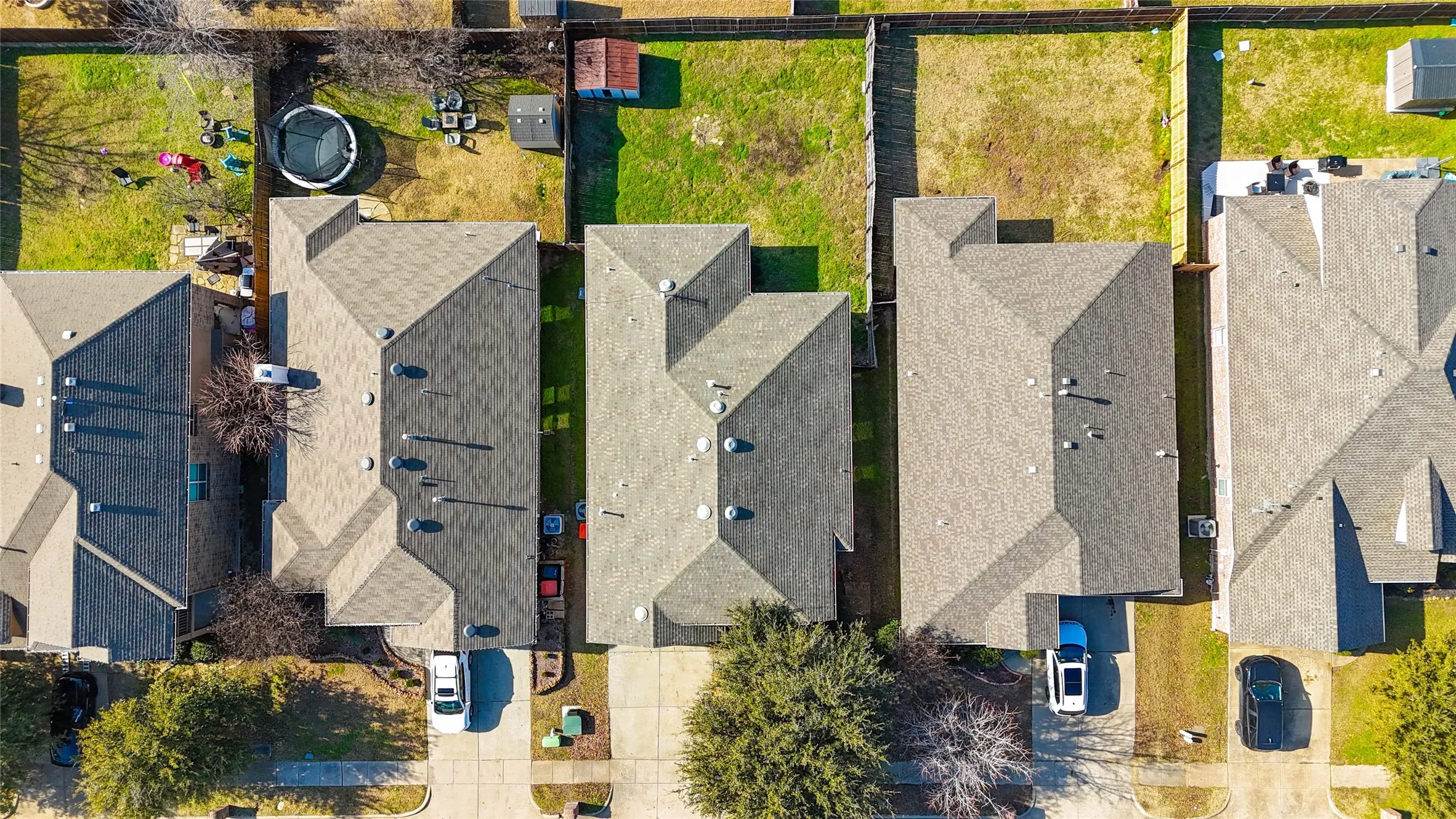 Overhead perspective showcasing a residential property with a shingled roof, a paved driveway, and established trees in the front yard