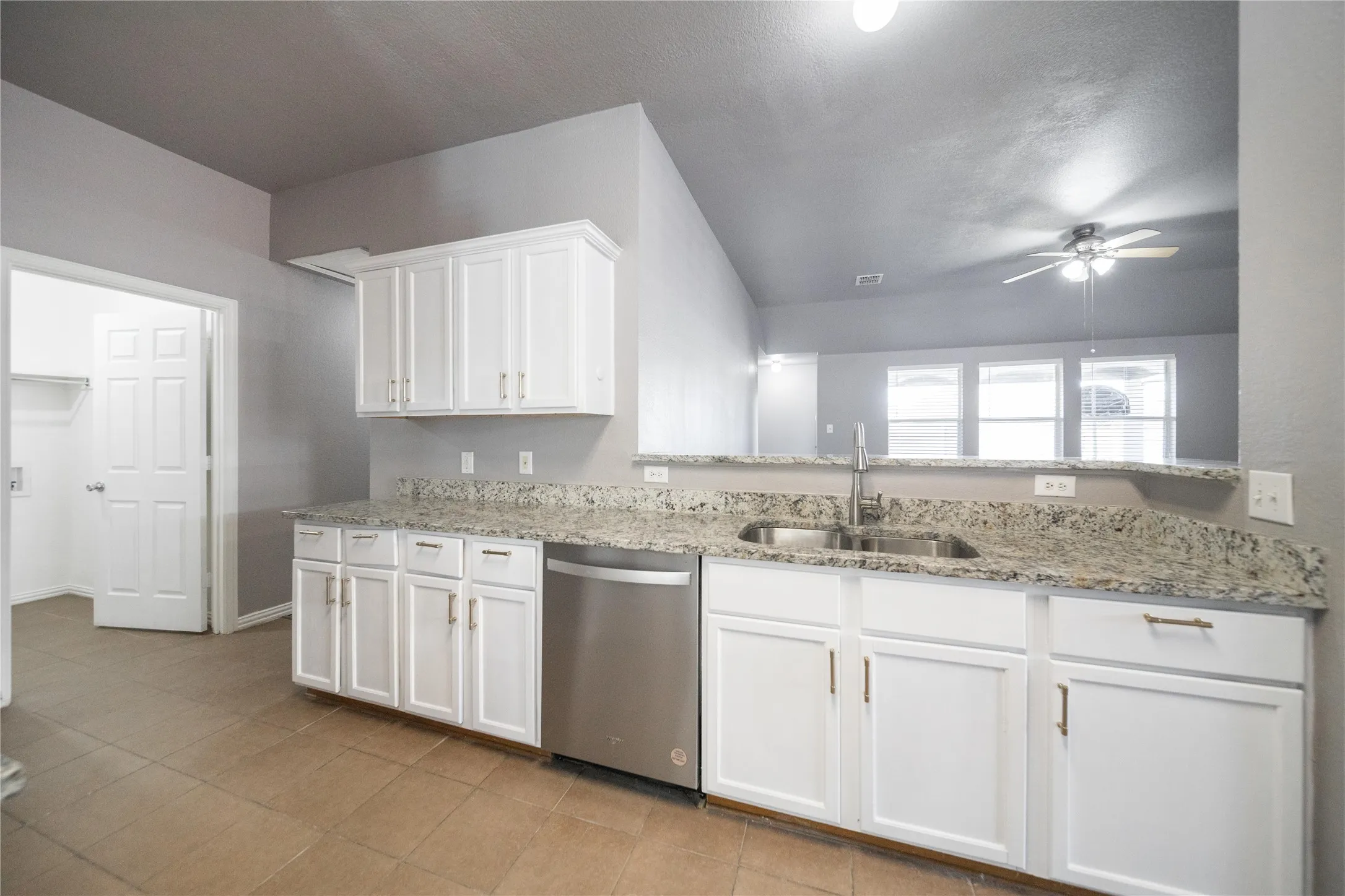 Kitchen featuring white cabinetry, a stainless steel dishwasher, a double basin stainless steel sink, and light granite countertops