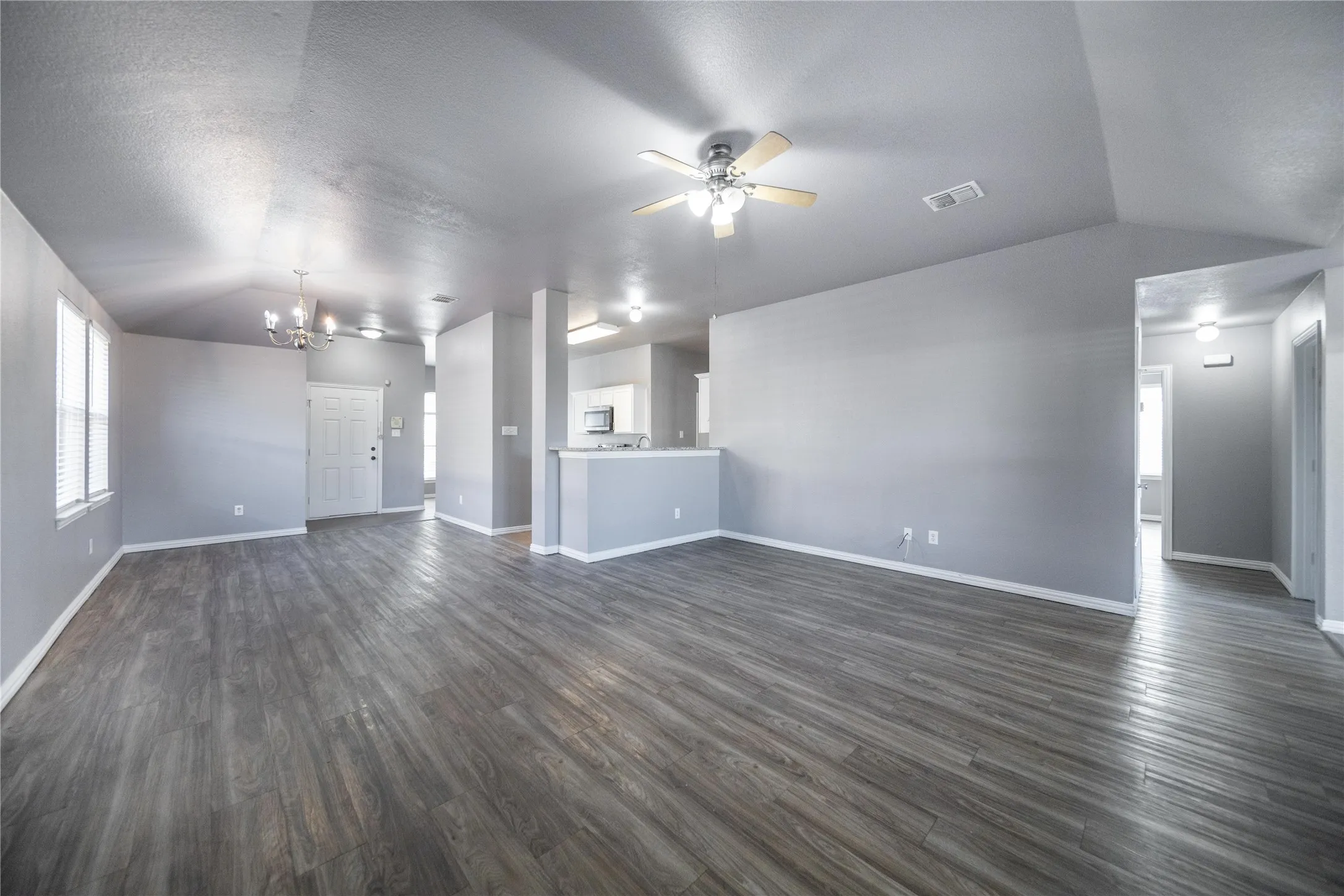 Spacious room featuring wood-finish flooring, vaulted ceilings, and light gray wall tones